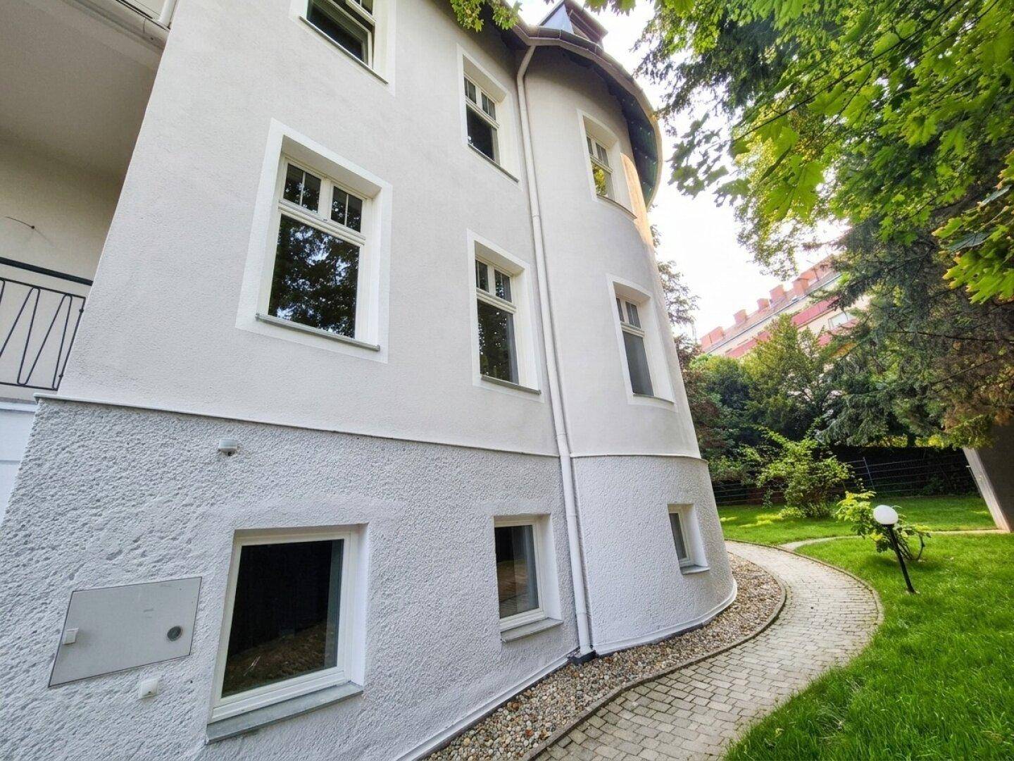 Attraktive Gebäudefassade mit geschwungenem Gartenweg und viel Grün.