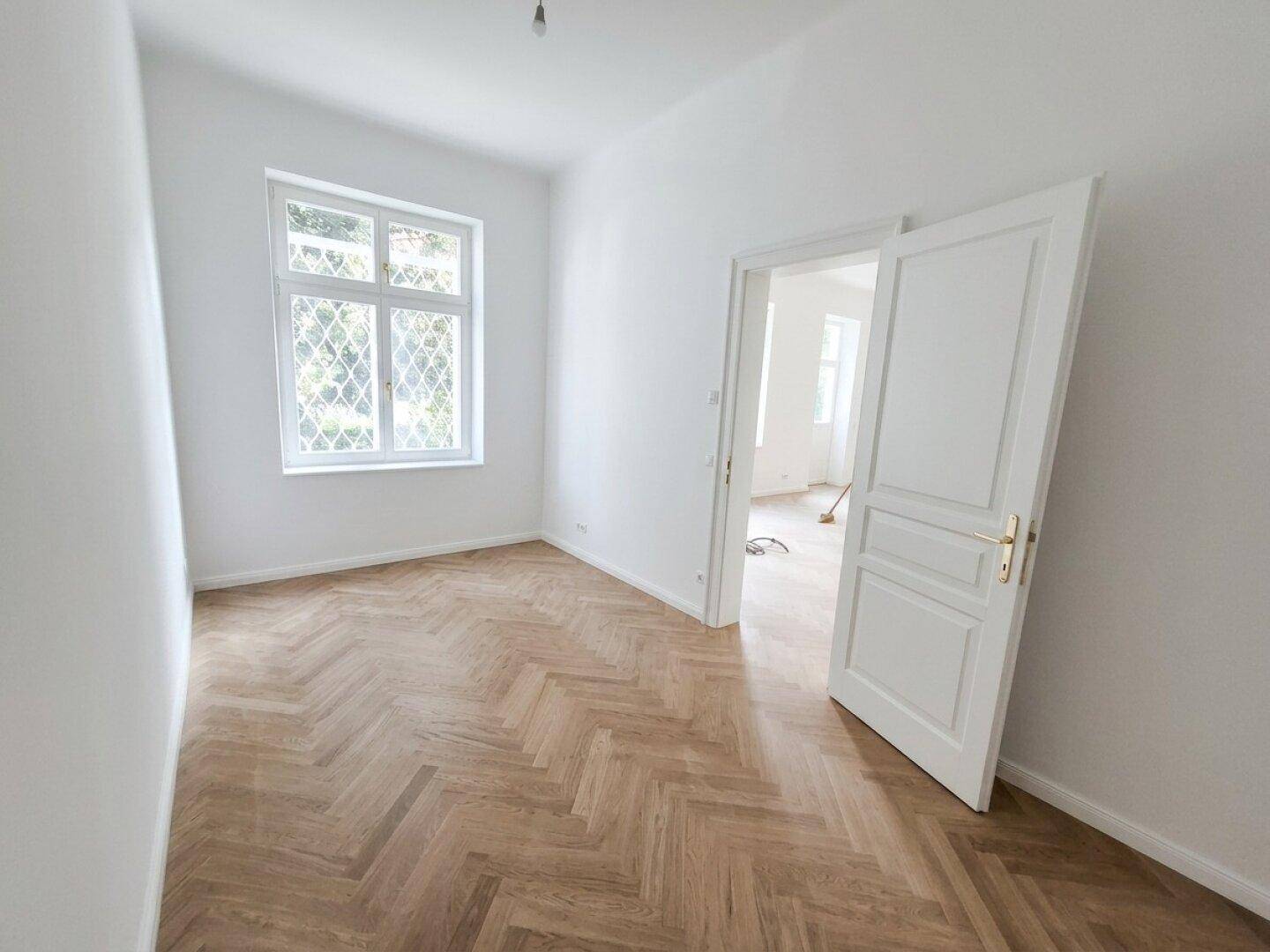 Helles Zimmer mit Fischgrätparkett und Flügeltür zu einem weiteren Wohnbereich.