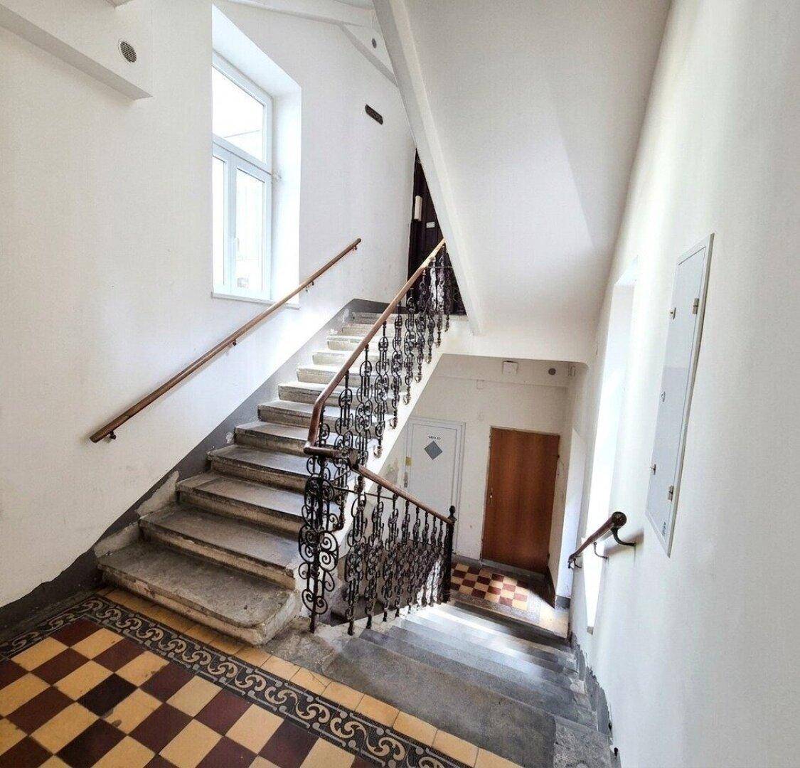 Historisches Treppenhaus mit schmiedeeisernem Geländer, Fliesenboden und natürlichem Lichteinfall.