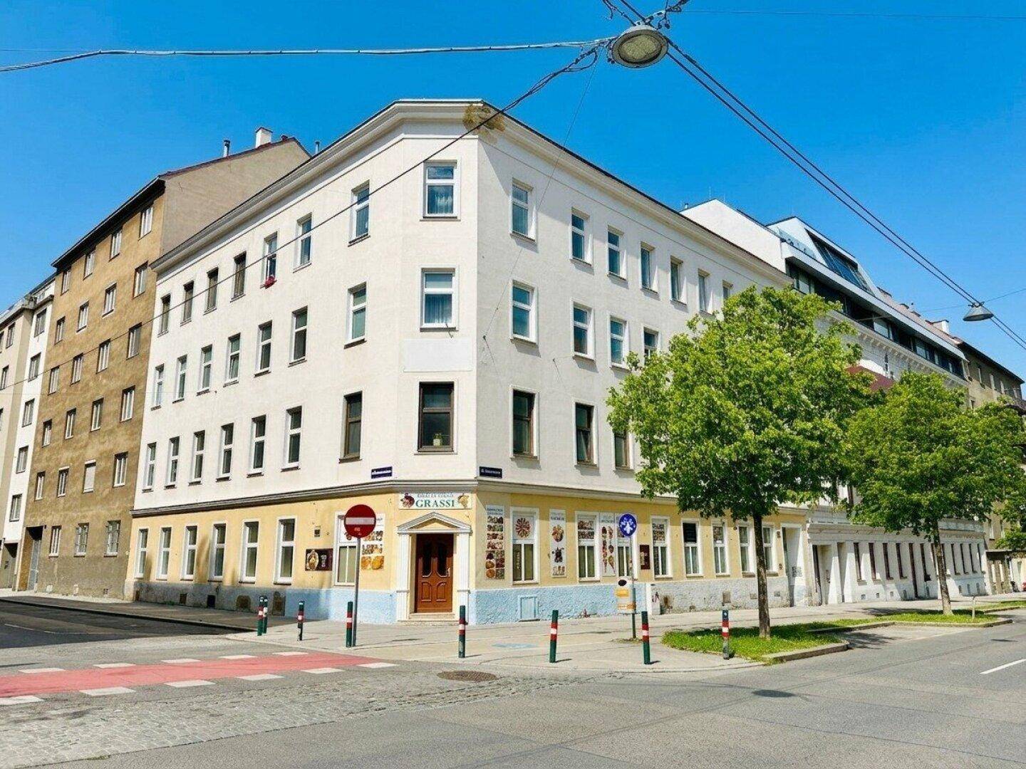 Eckgebäude mit Geschäften im Erdgeschoss an einer belebten Straßenkreuzung.