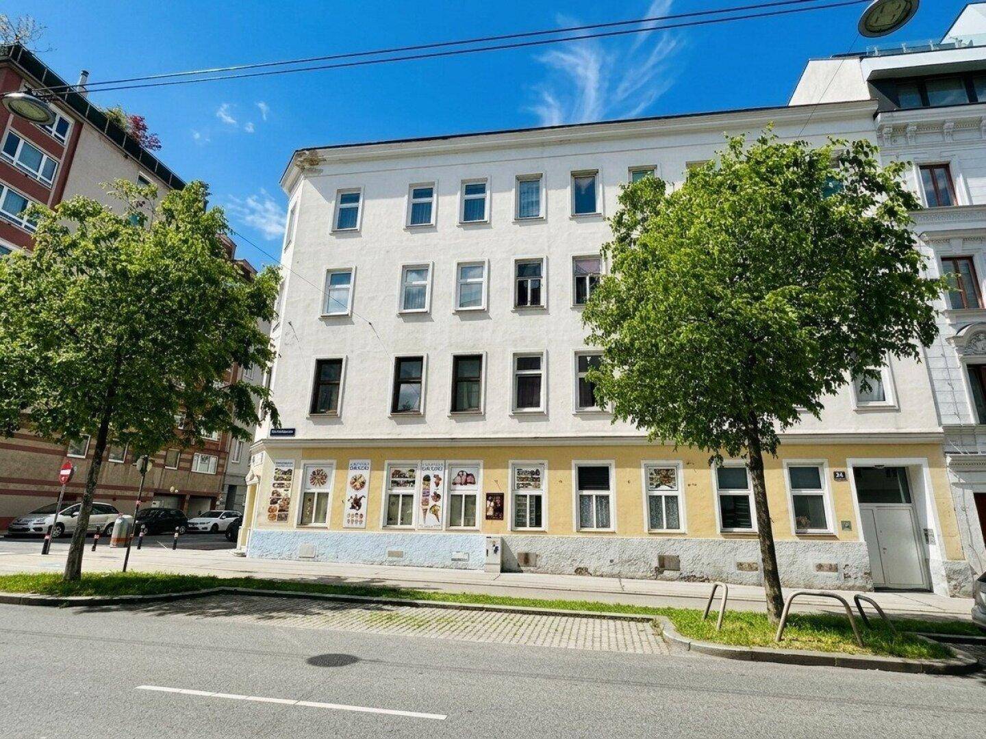 Gepflegte Fassade eines Mehrfamilienhauses in der Stadt mit großen Fenstern und Bäumen davor.