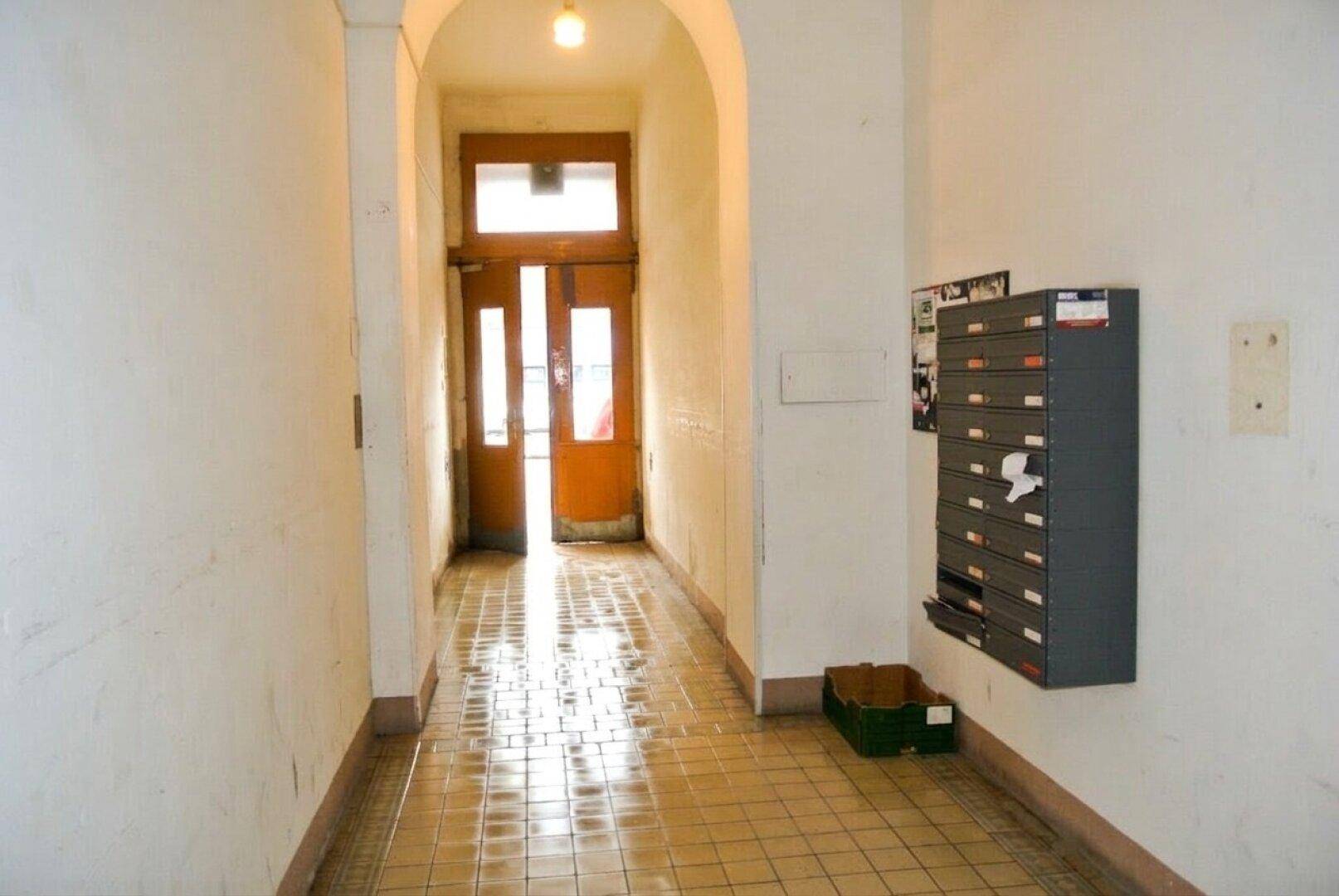 Langer Flur mit Fliesenboden, weißen Wänden und einem Eingangsbereich mit Briefkästen.