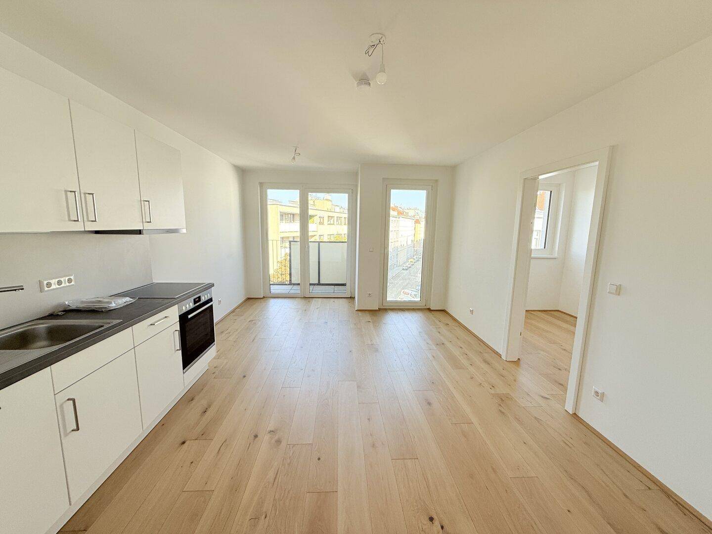 Offener Wohnbereich mit integrierter Küche, Holzboden und Zugang zu einem weiteren Raum.