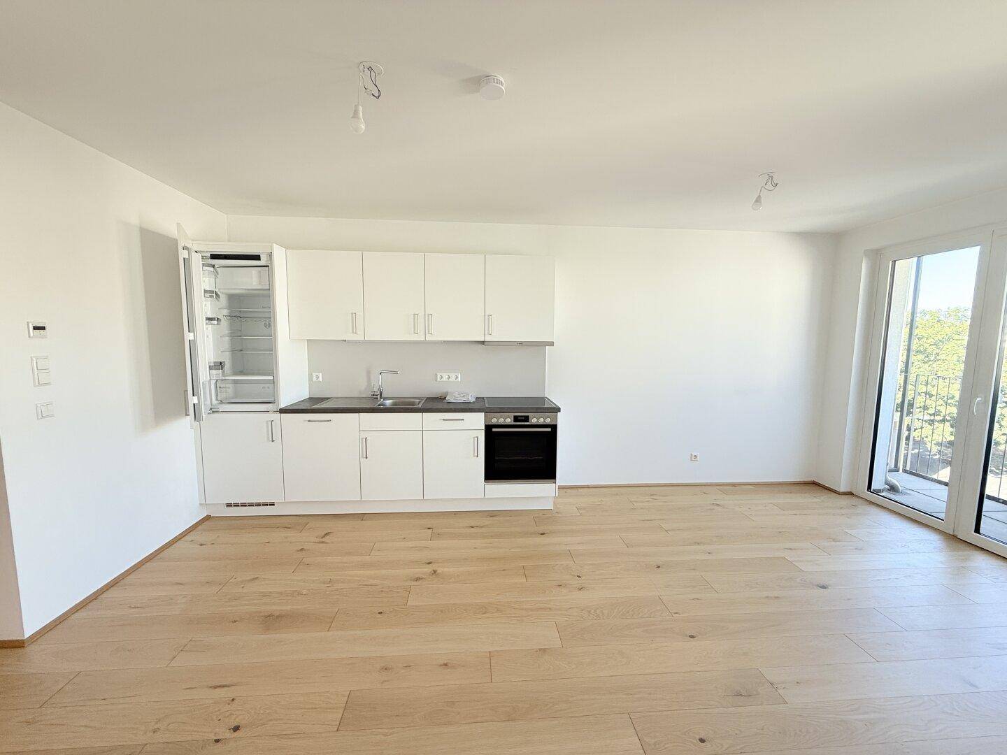 Geräumige Wohnküche mit heller Einrichtung, Holzboden und großen Fenstern für viel Tageslicht.