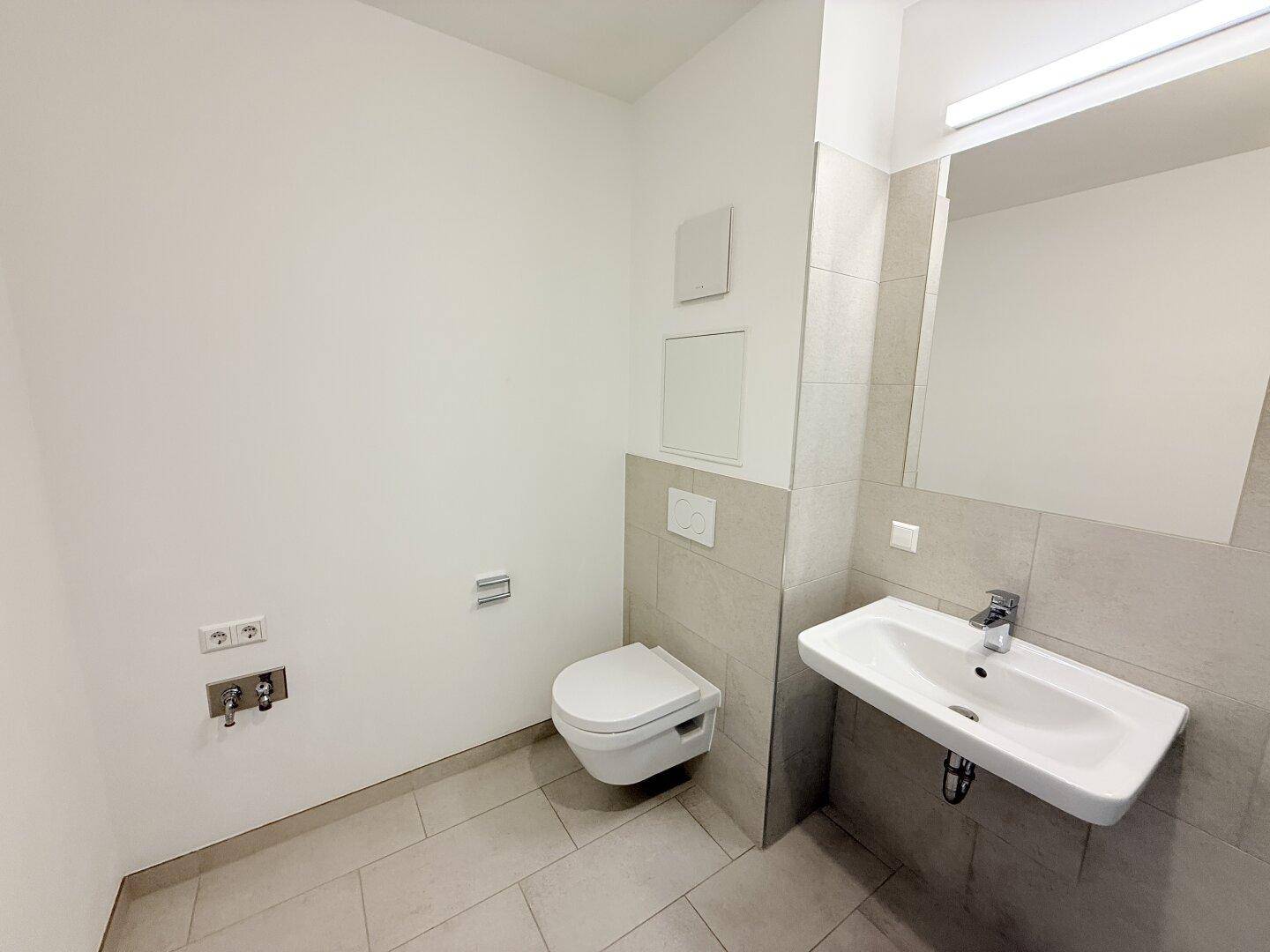 Zeitgemäßes Badezimmer mit WC, Waschbecken und hellen Fliesen, bereit für die Nutzung.