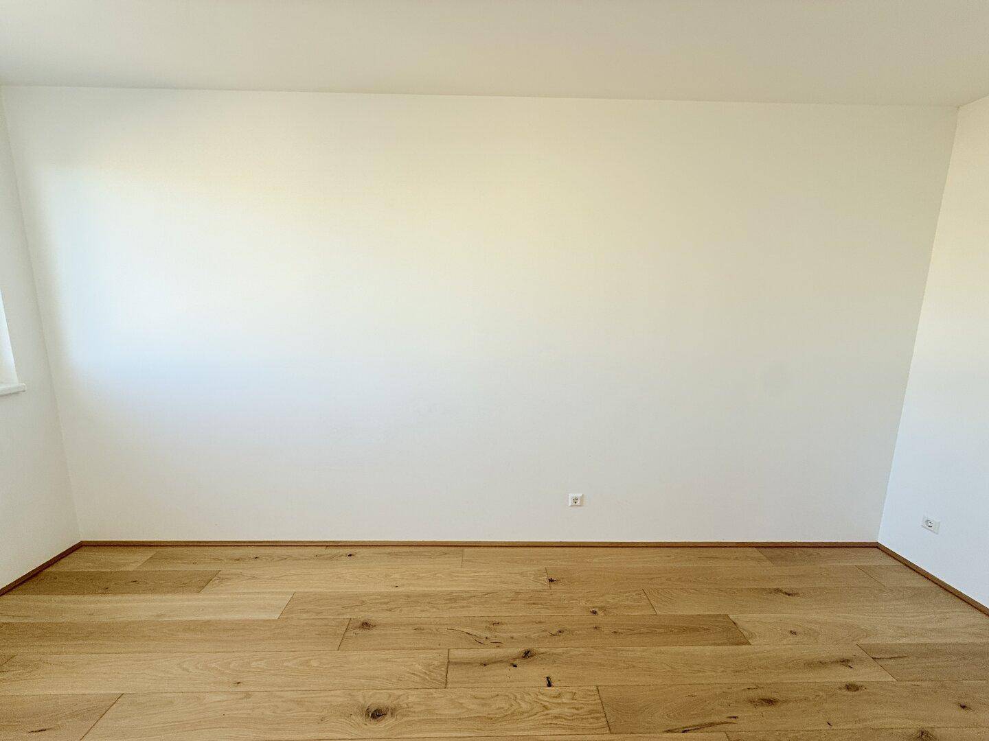 Leeres Zimmer mit hellem Holzboden und weißen Wänden, bereit zur individuellen Gestaltung.