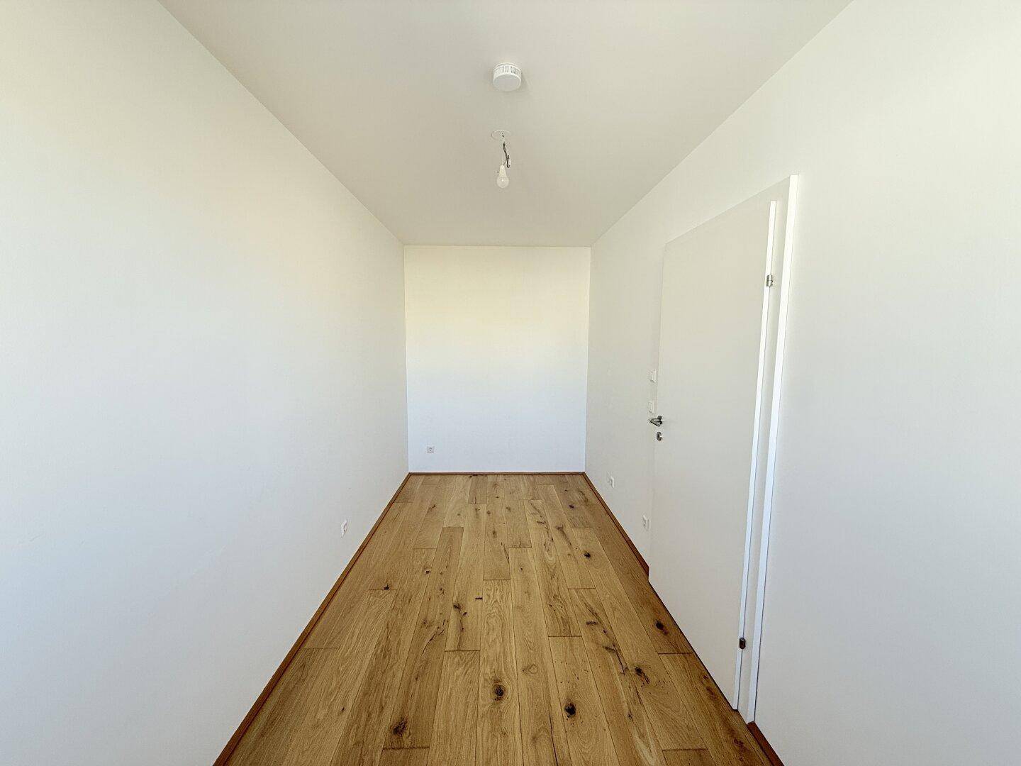 Langes, schmales Zimmer mit Holzboden und weiß gestrichenen Wänden, ideal als Schlafzimmer.