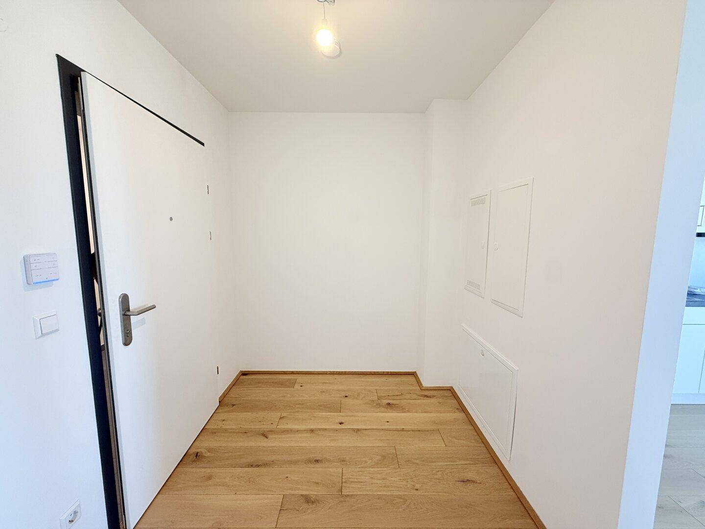 Heller Flur mit Holzboden und weißer Eingangstür, führt in den Wohnbereich der Wohnung.