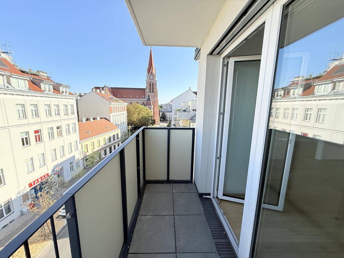 Schmaler Balkon mit Stadtblick und einer Kirche im Hintergrund unter blauem Himmel.