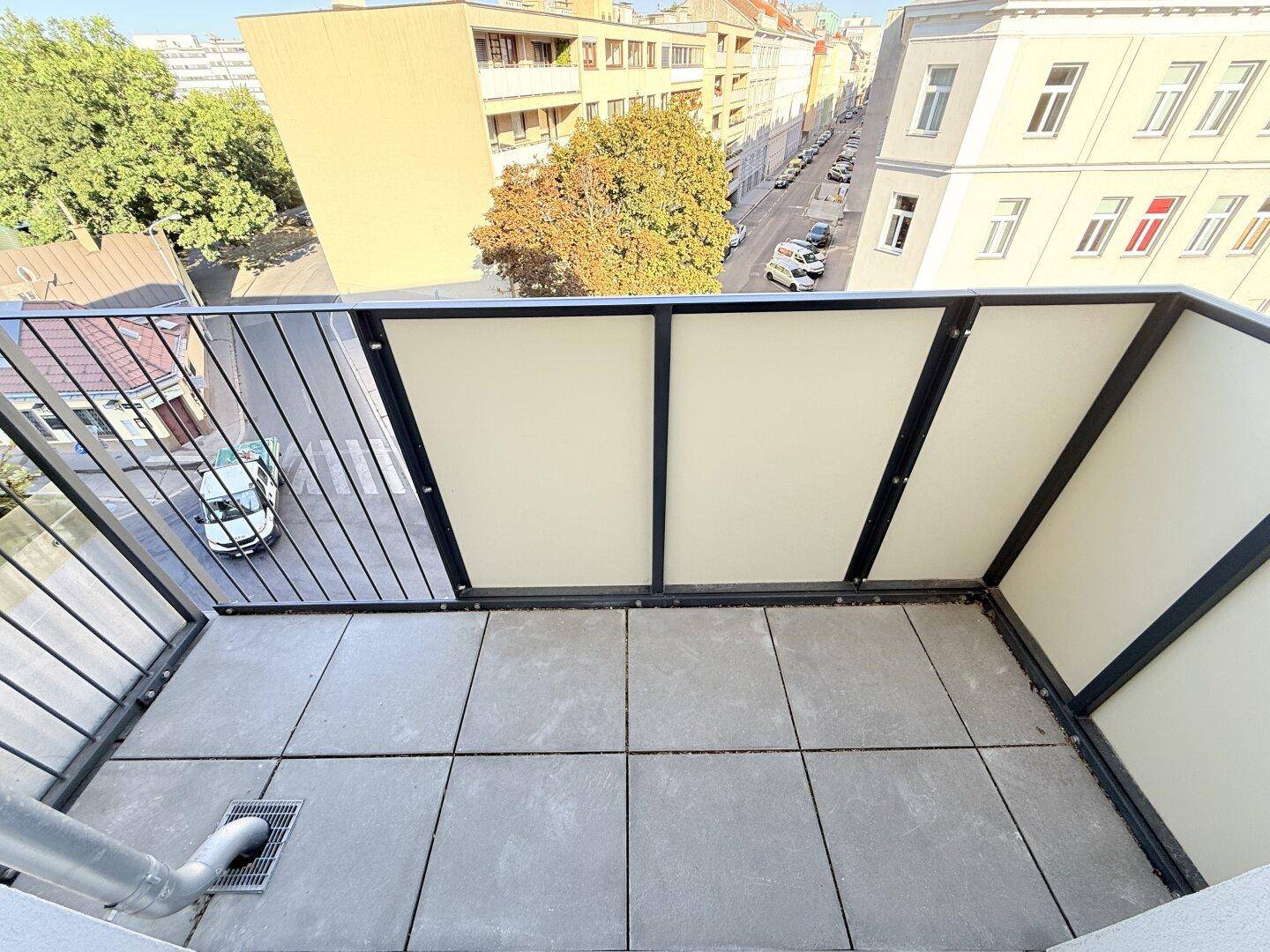 Kleiner Balkon mit Fliesenboden und Blick auf die umliegenden Gebäude und die Straße.