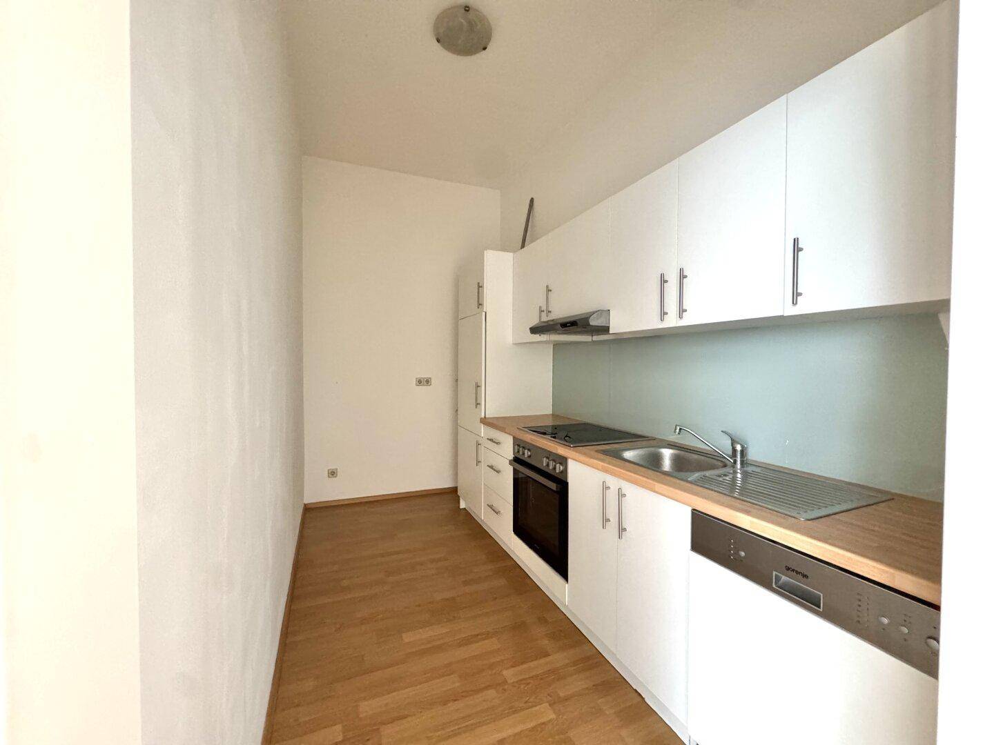 Funktionale Einbauküche mit weißen Schränken, Holztheke und integrierten Geräten.