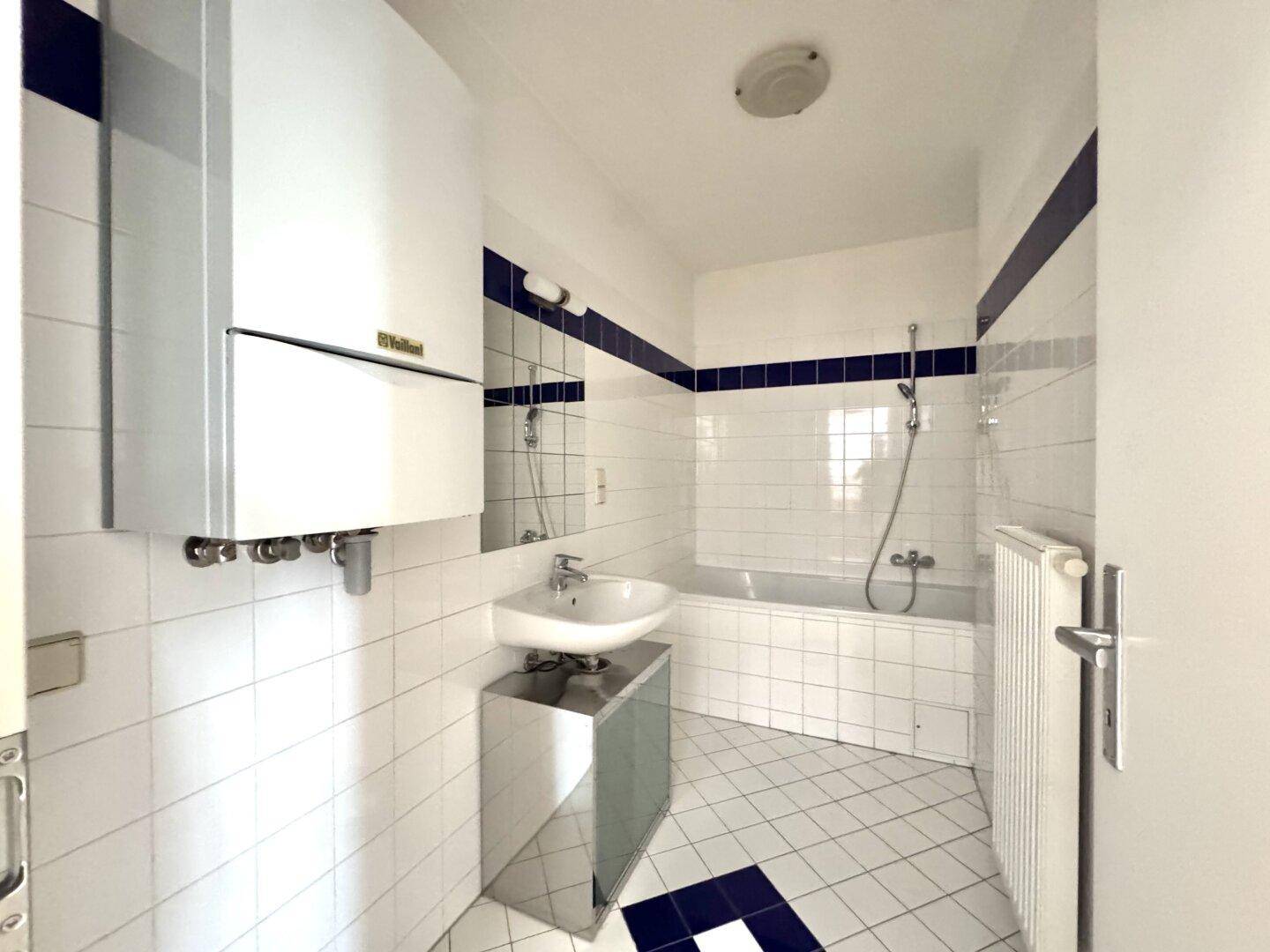 Badezimmer mit weißen Fliesen, Badewanne und Gastherme, in gutem Zustand.