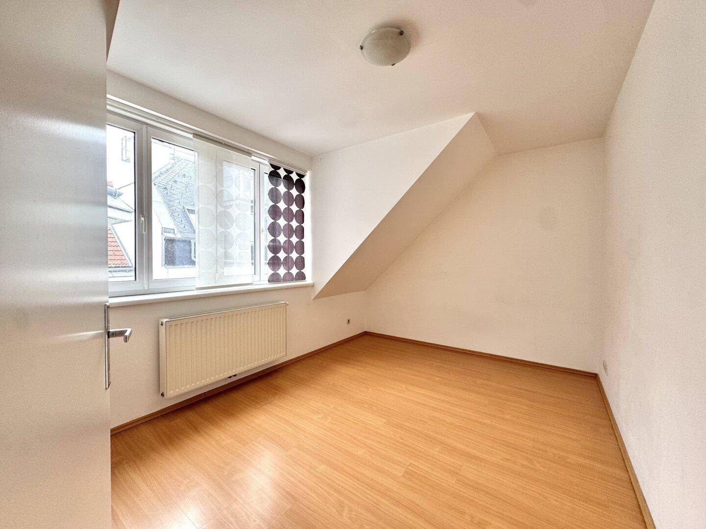 Gemütliches Zimmer mit Laminatboden, großem Fenster und Heizkörper, ideal als Schlafzimmer.