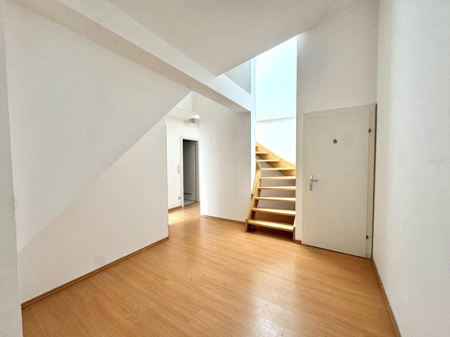 Heller Eingangsbereich mit Holztreppe und Laminatboden, führt zu den oberen Etagen.