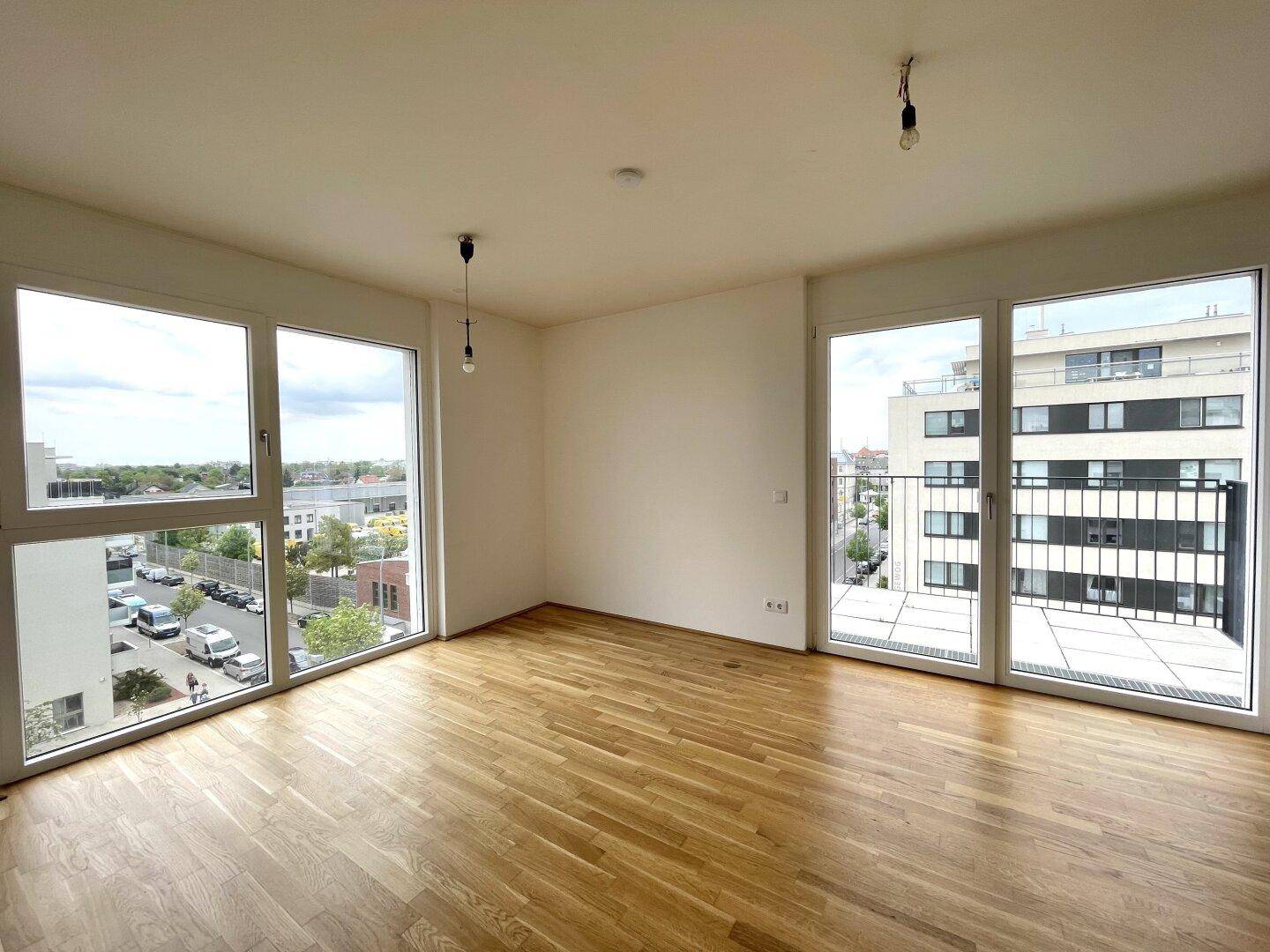 Heller Wohnraum mit großen Fenstern, Parkettboden und direktem Zugang zum Balkon.
