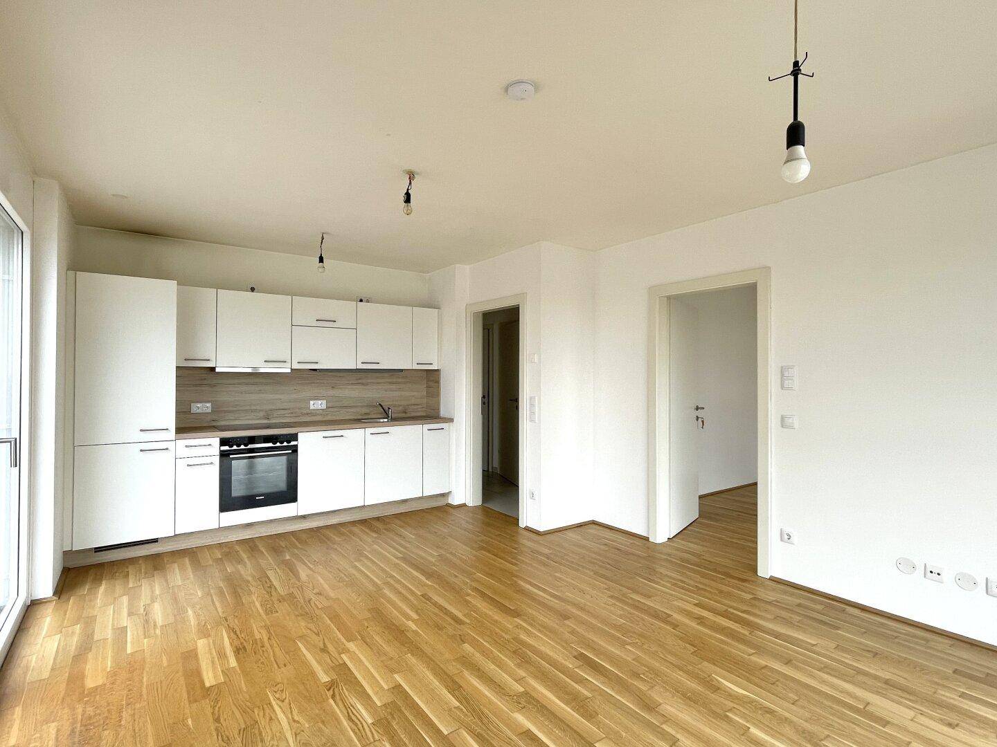 Moderne offene Wohnküche mit weißen Schränken, Holzboden und integriertem Backofen.