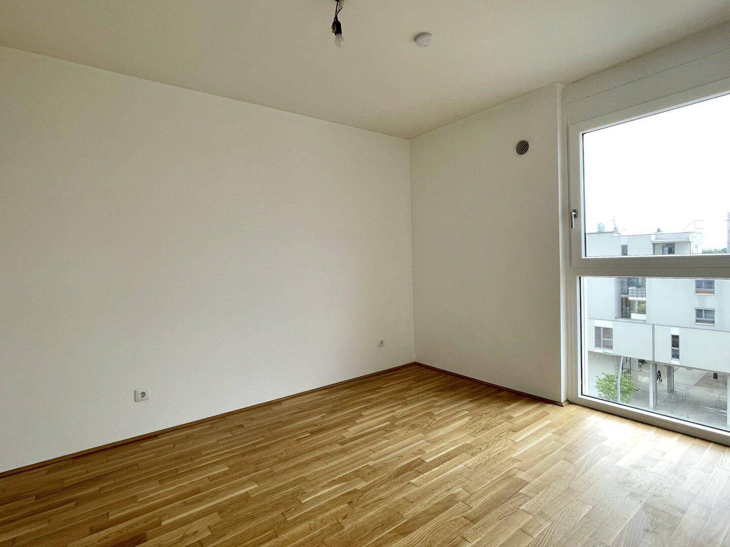 Geräumiges Schlafzimmer mit hellem Parkettboden und einem hohen Fenster für gute Belichtung.