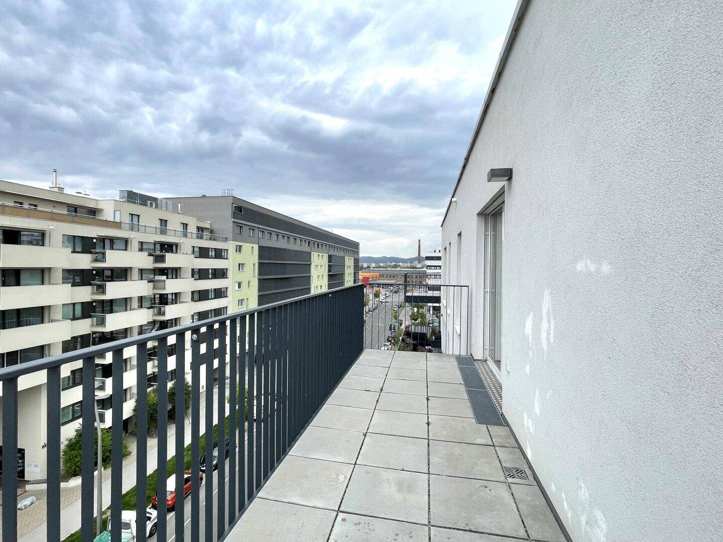 Langer Balkon mit Fliesenboden und Metallgeländer, bietet Ausblick auf die moderne Wohnbebauung.
