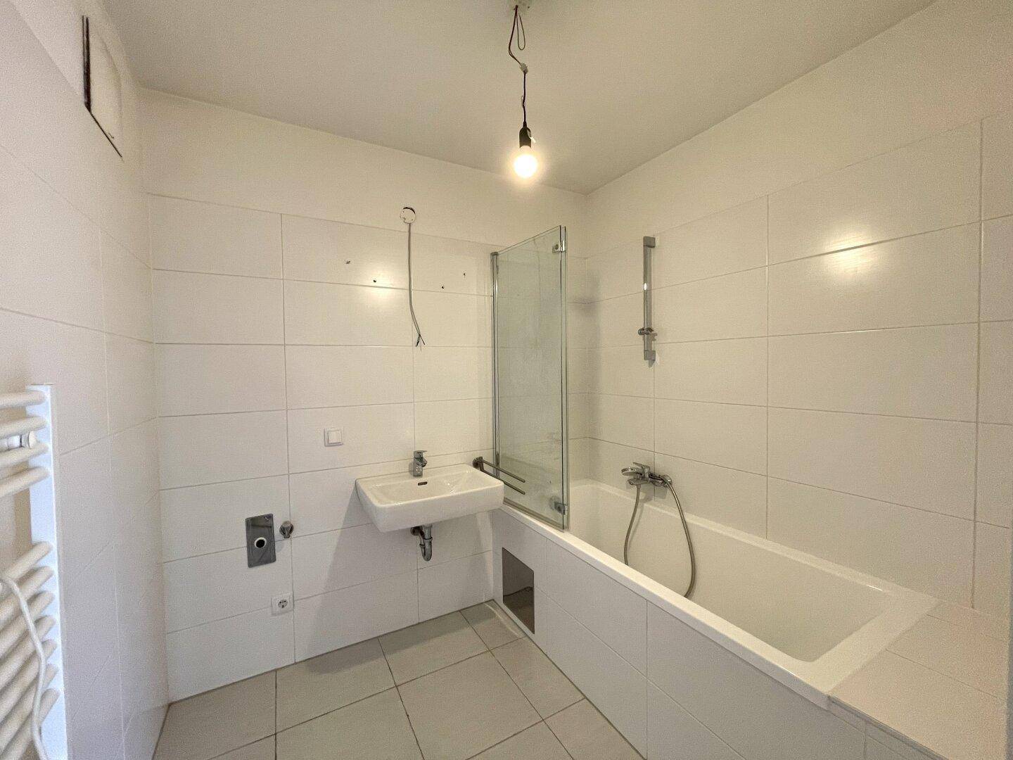 Modernes Badezimmer mit weißen Fliesen, Badewanne mit Duschwand und beheiztem Handtuchhalter.