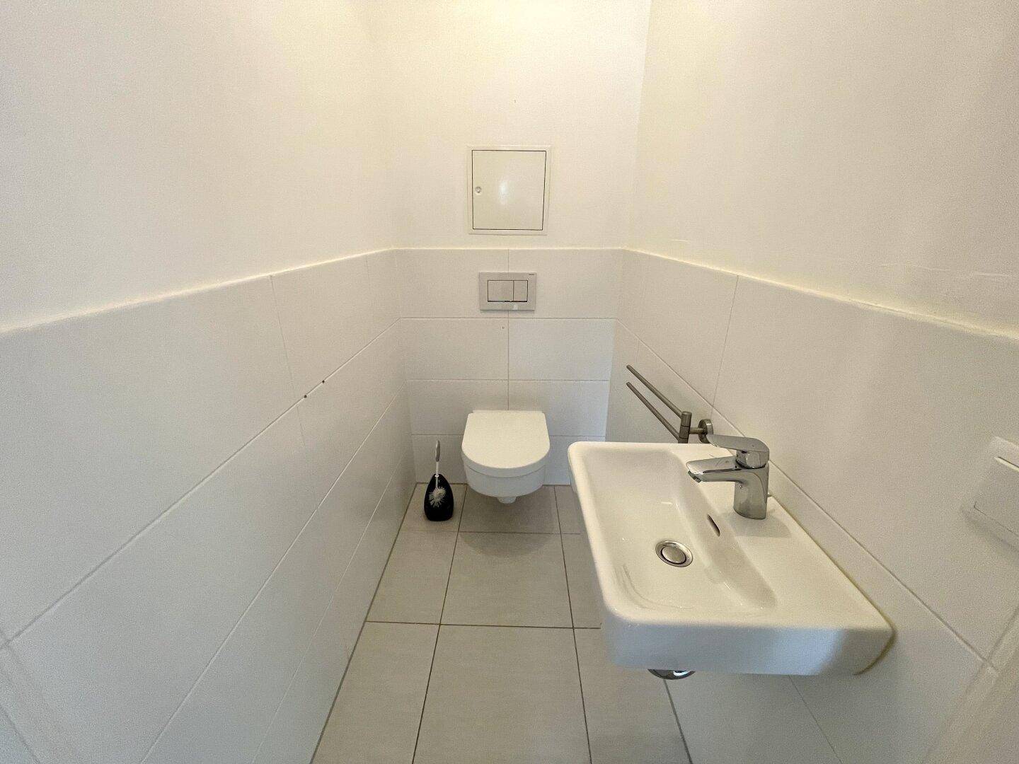Separates Gäste-WC mit wandhängender Toilette, kleinem Waschbecken und weißen Fliesen.