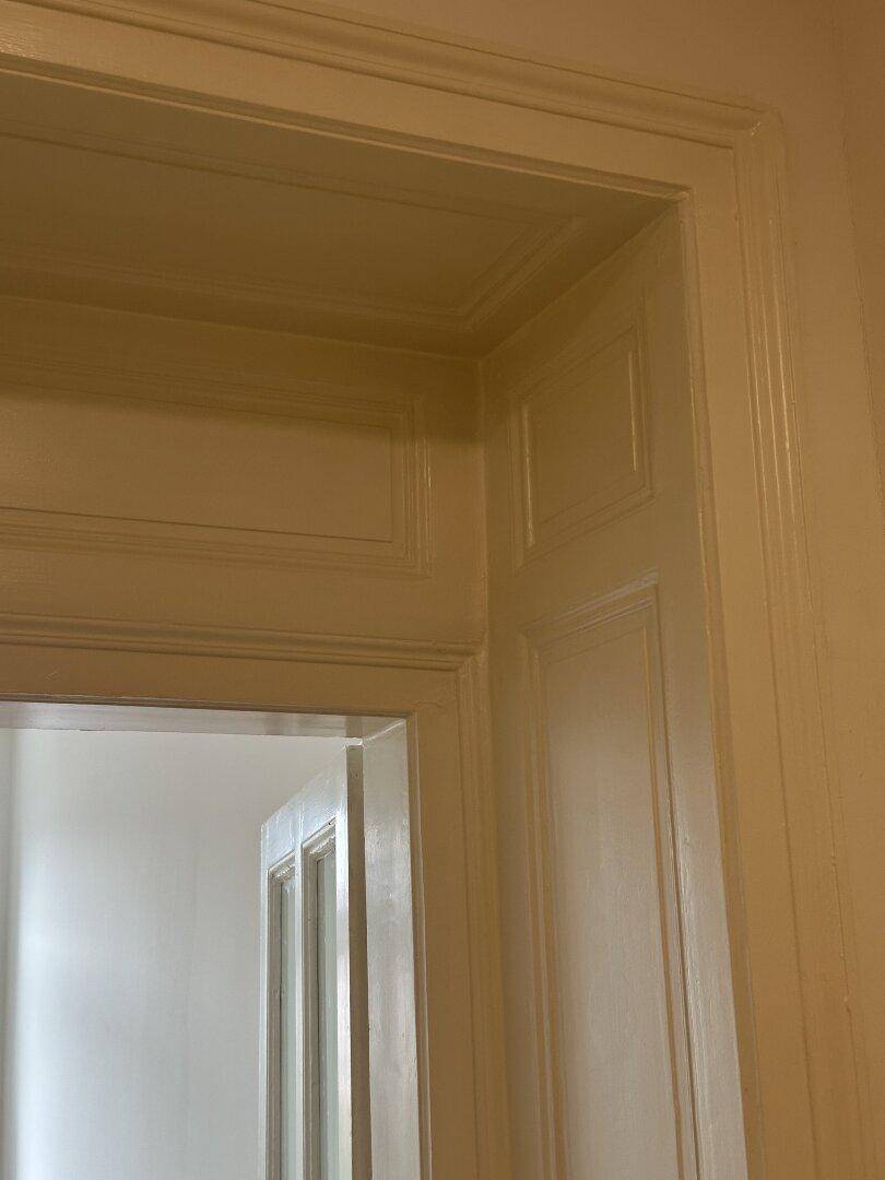 Detailaufnahme eines verzierten Türrahmens und einer Tür im klassischen Altbaustil.