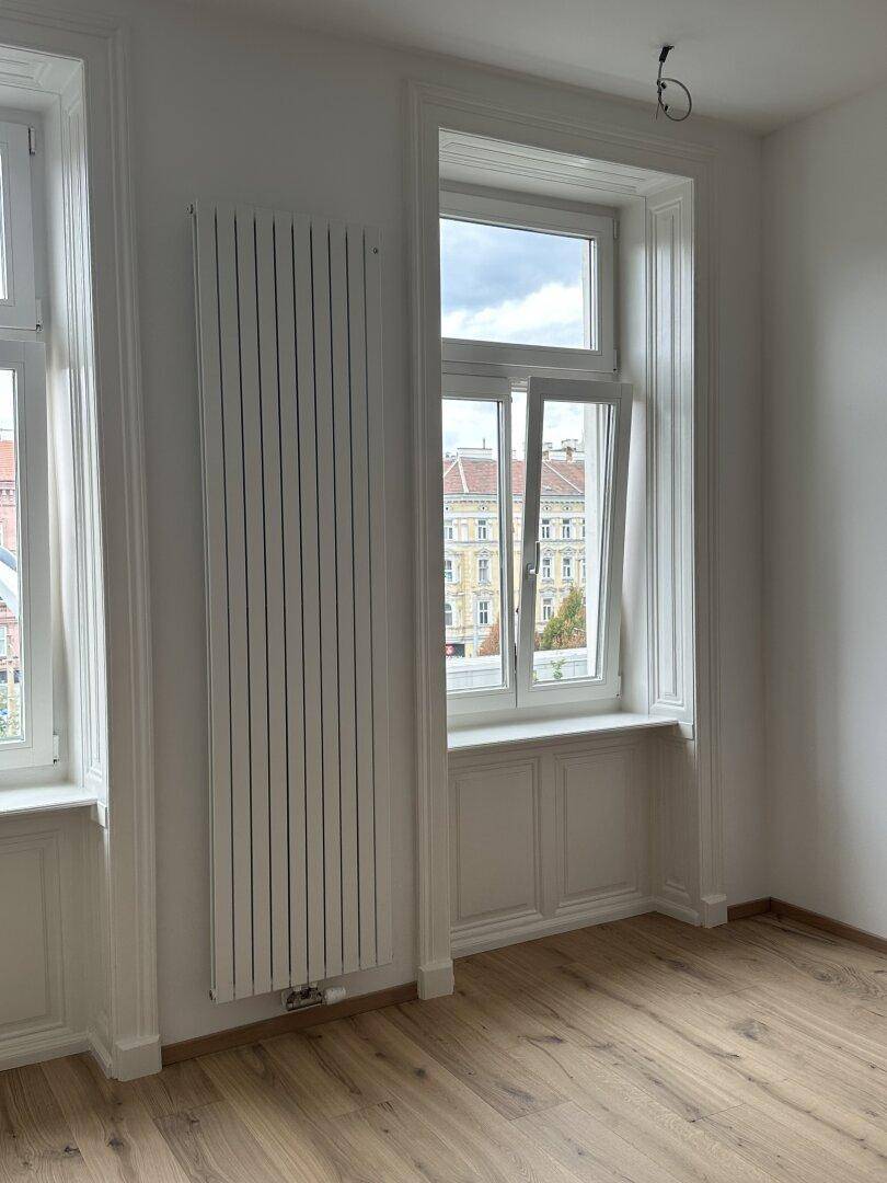 Helles Zimmer mit Holzboden, Heizkörper und Ausblick auf die Stadt.