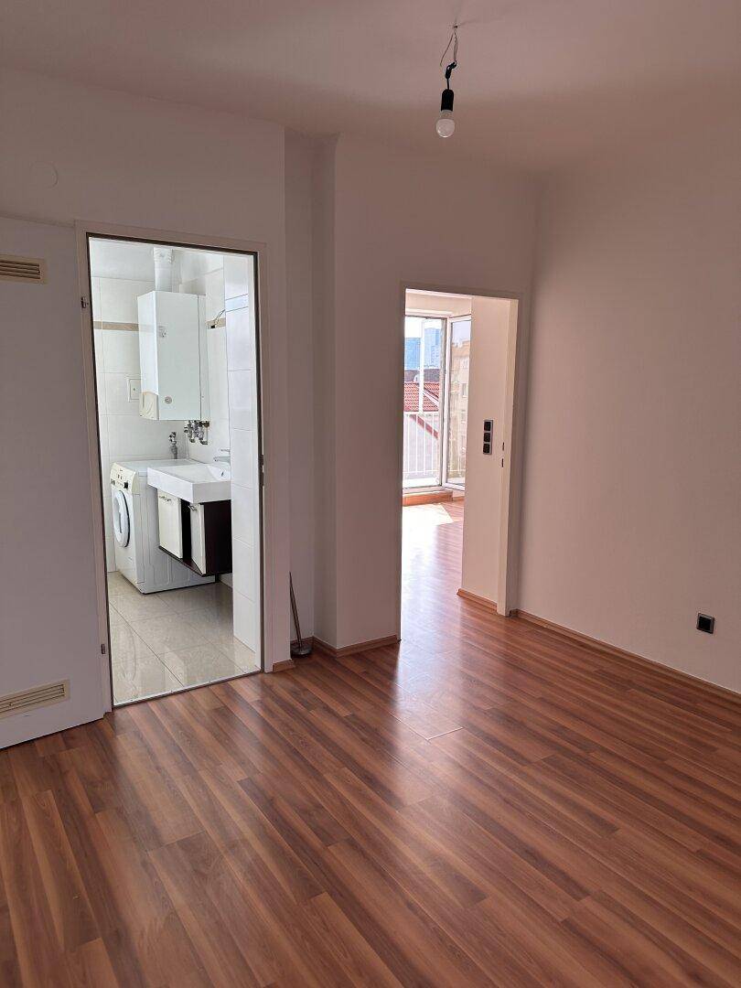 Heller Raum mit Laminatboden und Zugängen zu Bad und weiterem Zimmer mit Balkon.