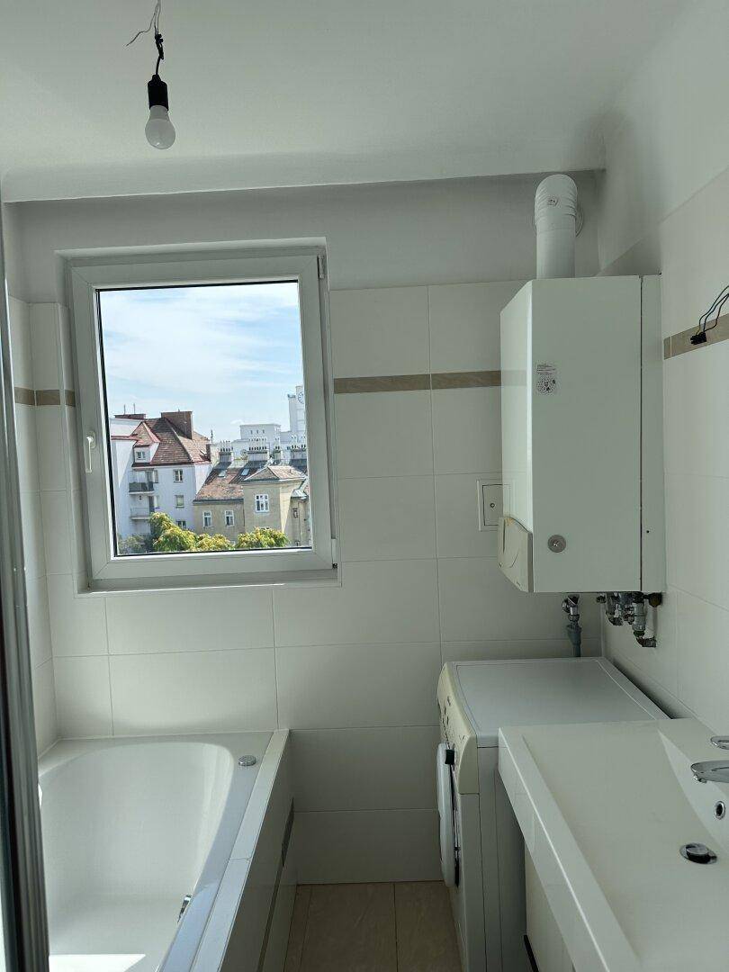 Badezimmer mit Badewanne, Waschbecken, Fenster und einem Wandheizkessel.
