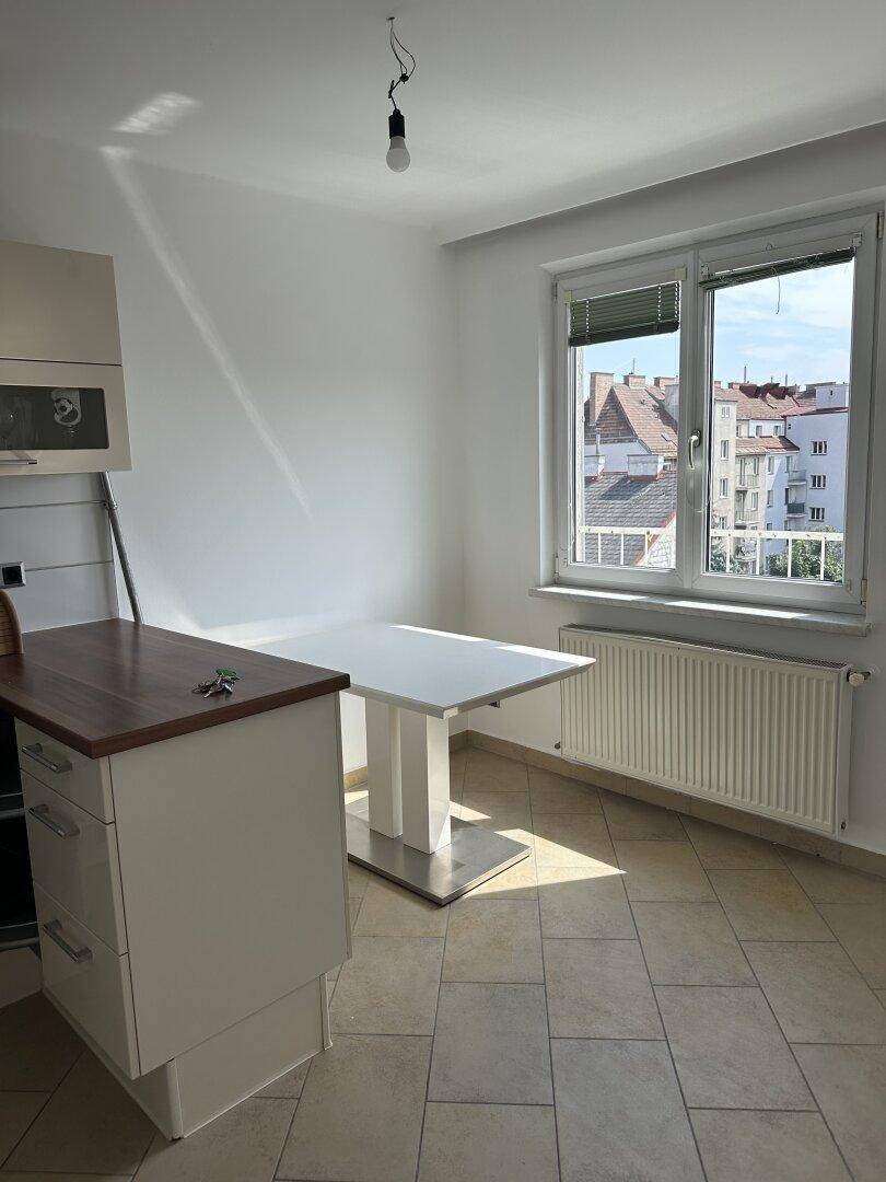 Helle Küchenzeile mit Fliesenboden, Esstisch und Fenster mit Blick auf die Dächer.
