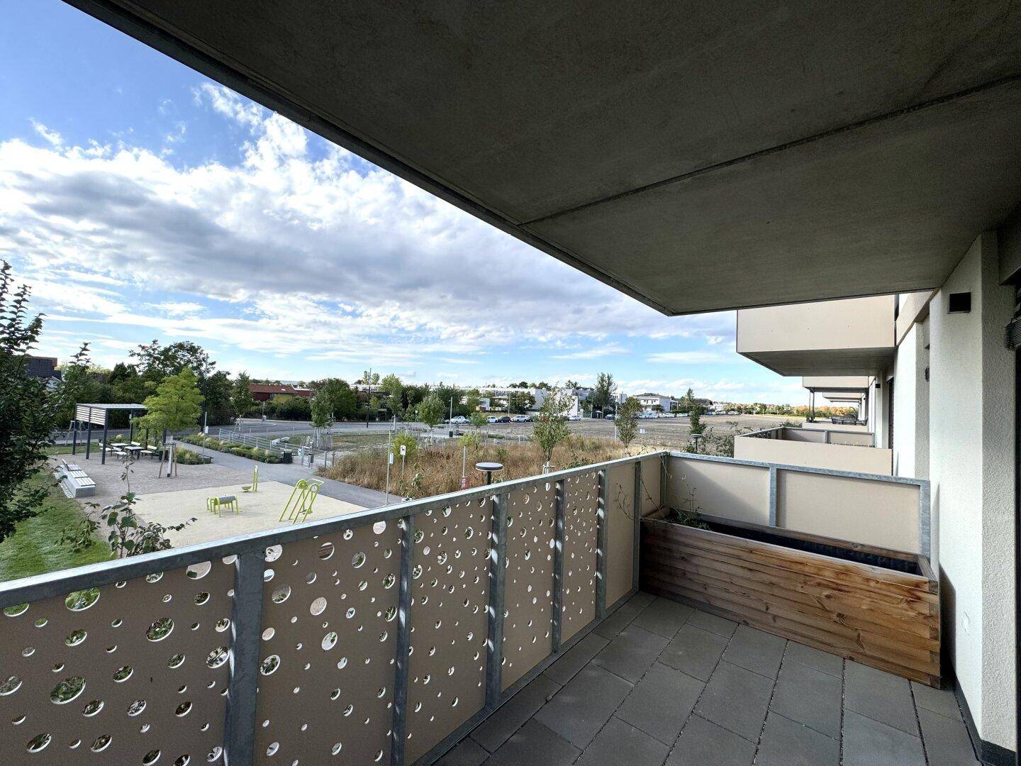 Geräumiger Balkon mit modernem Geländer, Fliesenboden und Blick auf die grüne Umgebung.
