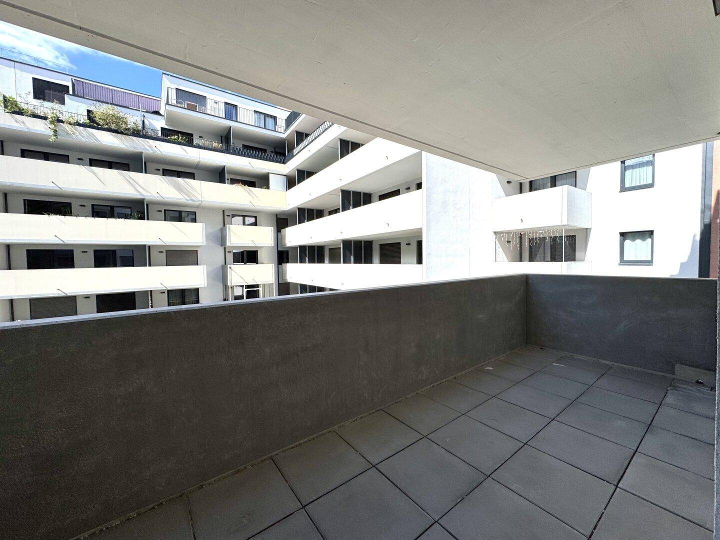 Geräumiger Balkon mit Fliesenboden und Blick auf die umliegenden modernen Wohngebäude.