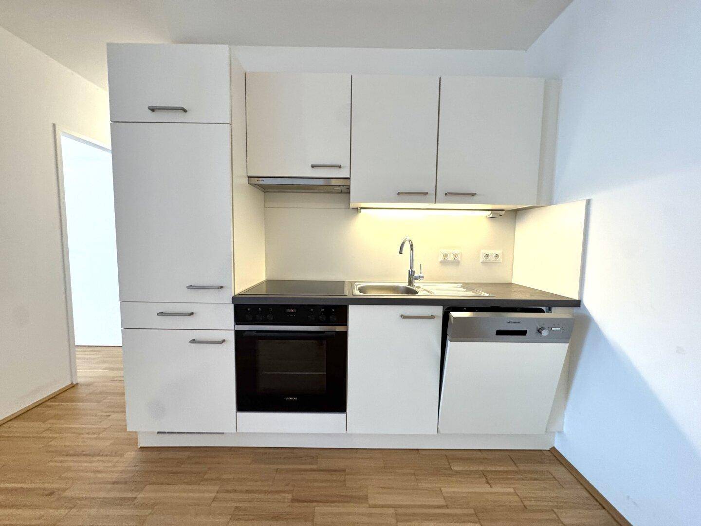 Moderne, kompakte Küchenzeile mit weißen Schränken, integriertem Backofen und Geschirrspüler.