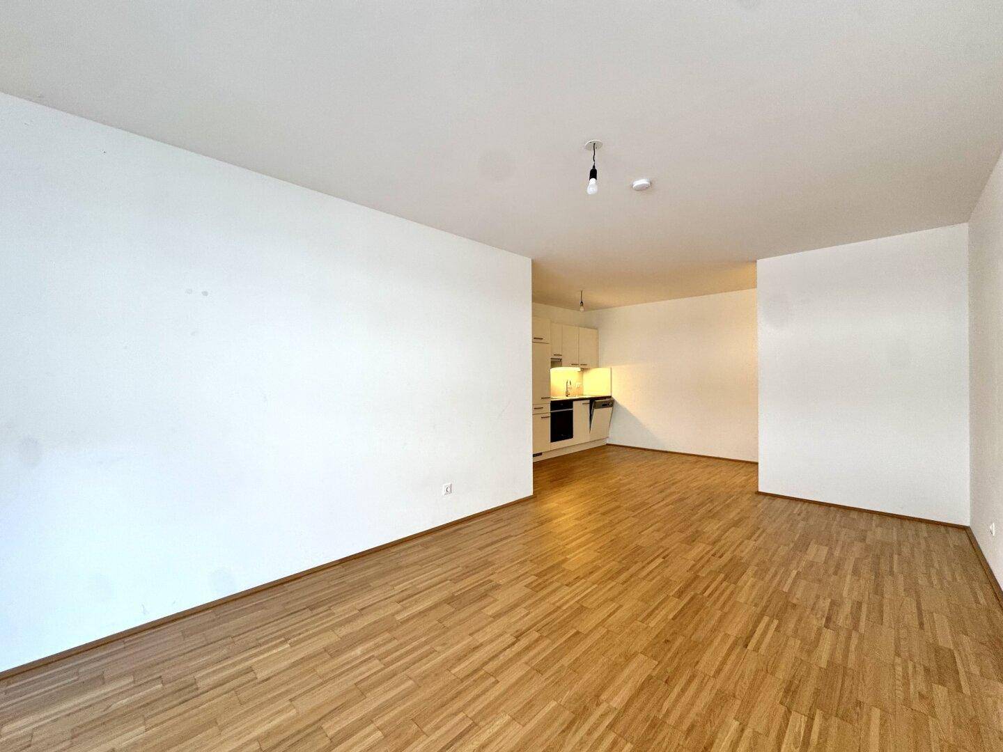 Geräumiger, offener Wohnbereich mit hellem Parkettboden und Blick auf die integrierte Küchenzeile.