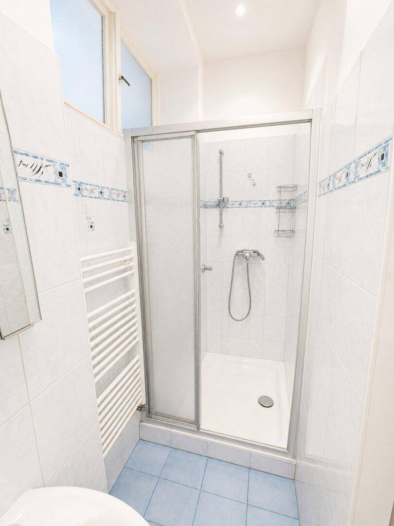 Helles Badezimmer mit Duschkabine, blauen Fliesen und praktischem Handtuchheizkörper.