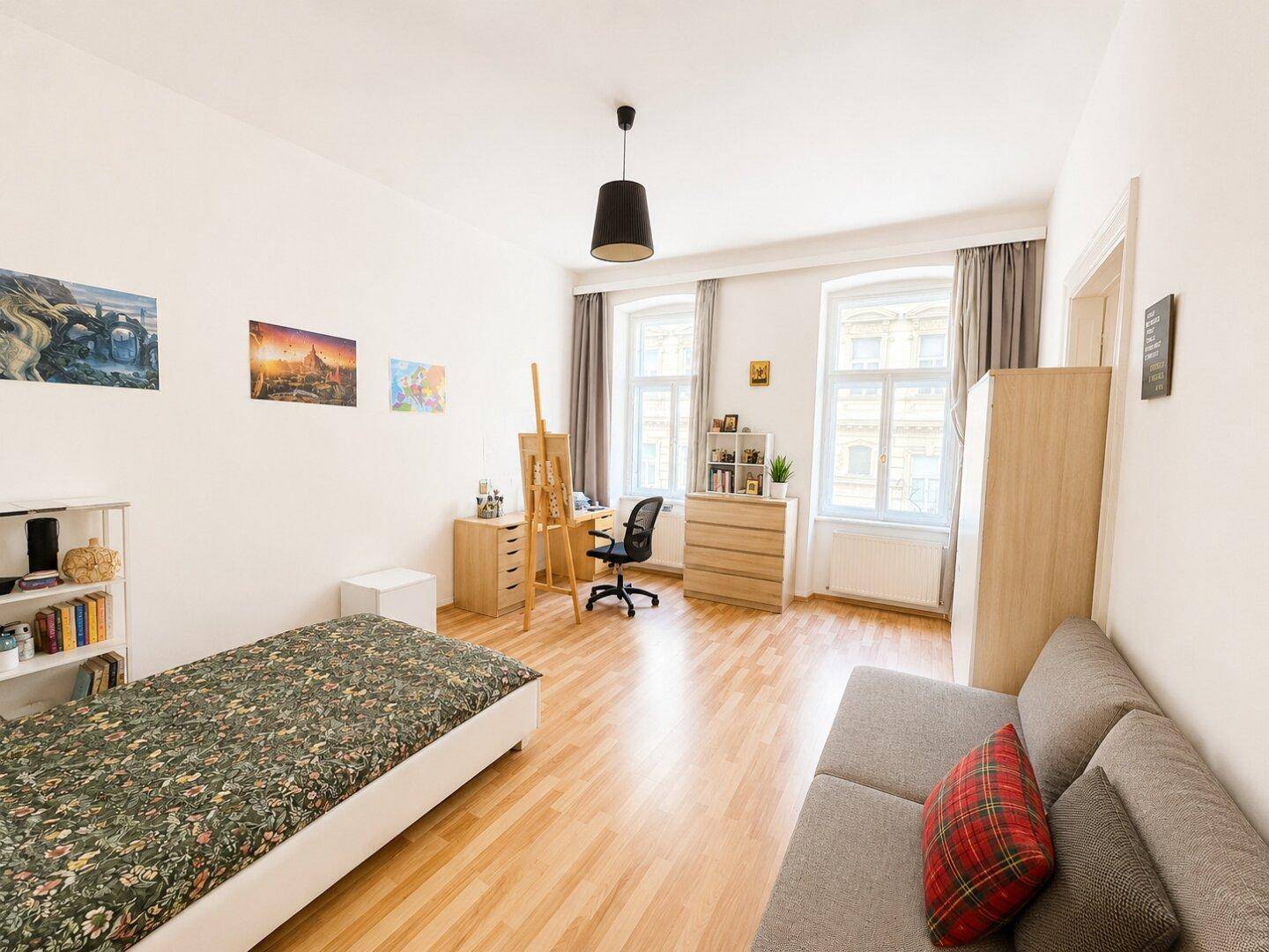 Geräumiges Schlafzimmer mit Holzboden, Schreibtisch und Sofa, hell und modern eingerichtet.