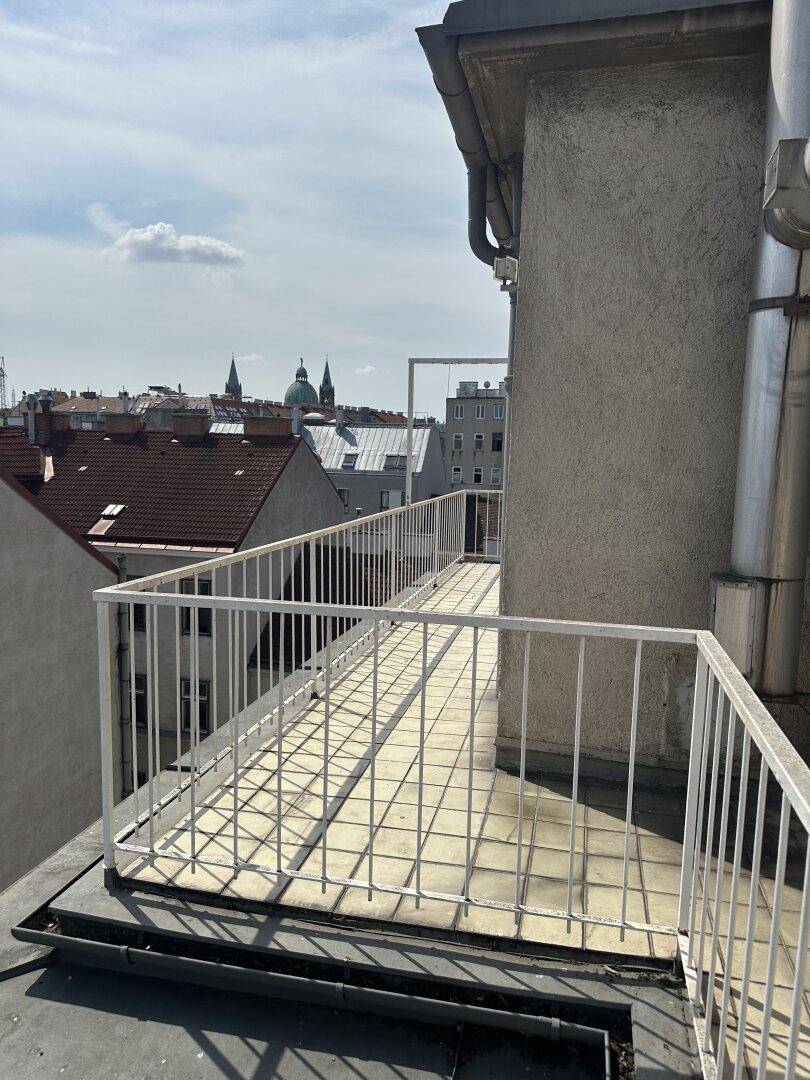 Langer, schmaler Balkon mit weißem Geländer und Blick über die Dächer der Stadt.