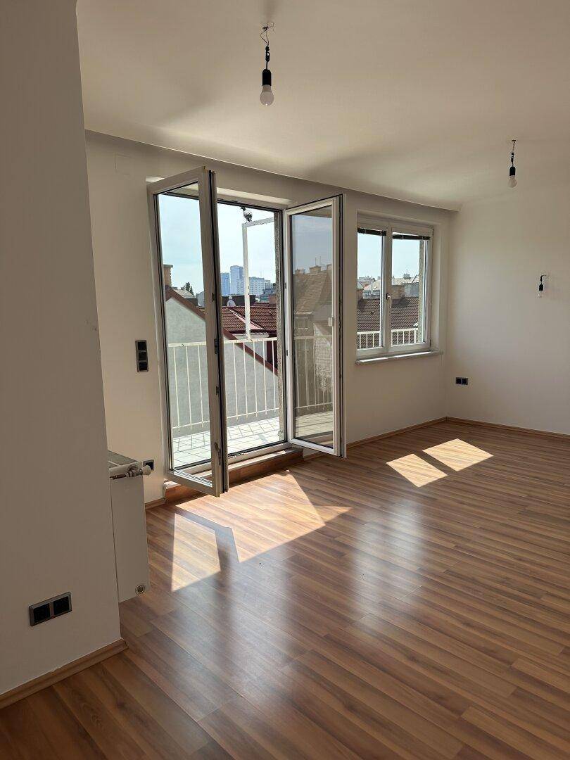 Helles Zimmer mit Holzboden, großen Falttüren zum Balkon und viel natürlichem Licht.