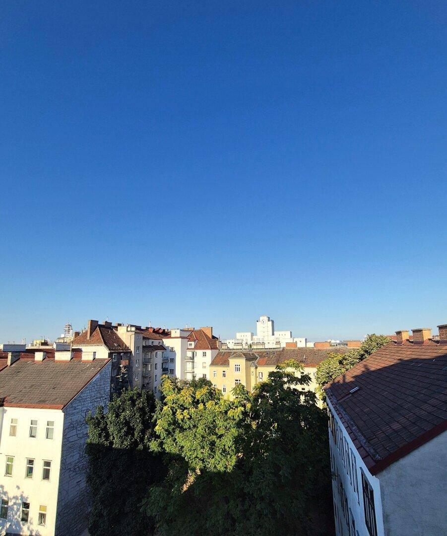 Panoramablick über die Dächer der Stadt mit grünen Bäumen unter einem strahlend blauen Himmel.