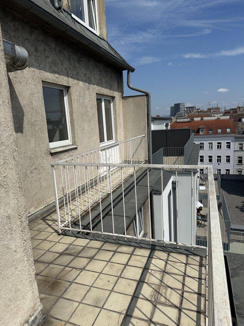 Balkon mit weißem Geländer und Blick auf die umliegenden Gebäude unter blauem Himmel.