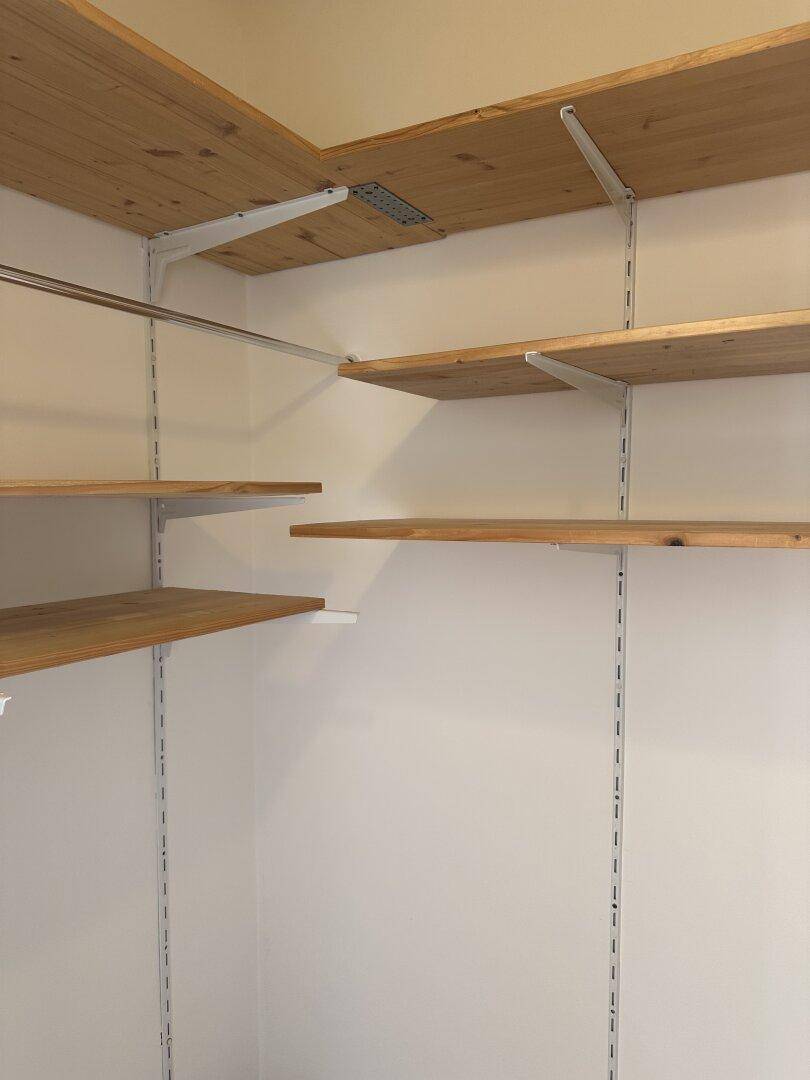 Praktischer Abstellraum mit verstellbaren Holzregalen und Kleiderstange für Stauraum.