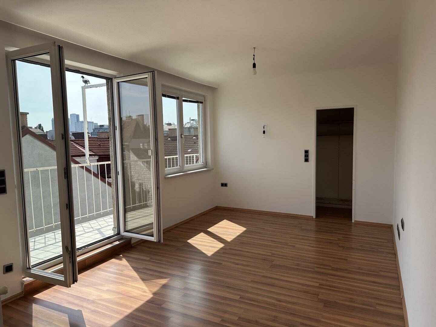 Lichtdurchfluteter Raum mit Laminatboden und Zugang zu einem Balkon, ideal als Wohnbereich.
