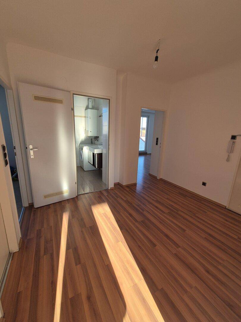 Heller Raum mit Laminatboden und Zugängen zu Bad und weiterem Zimmer mit Balkon.