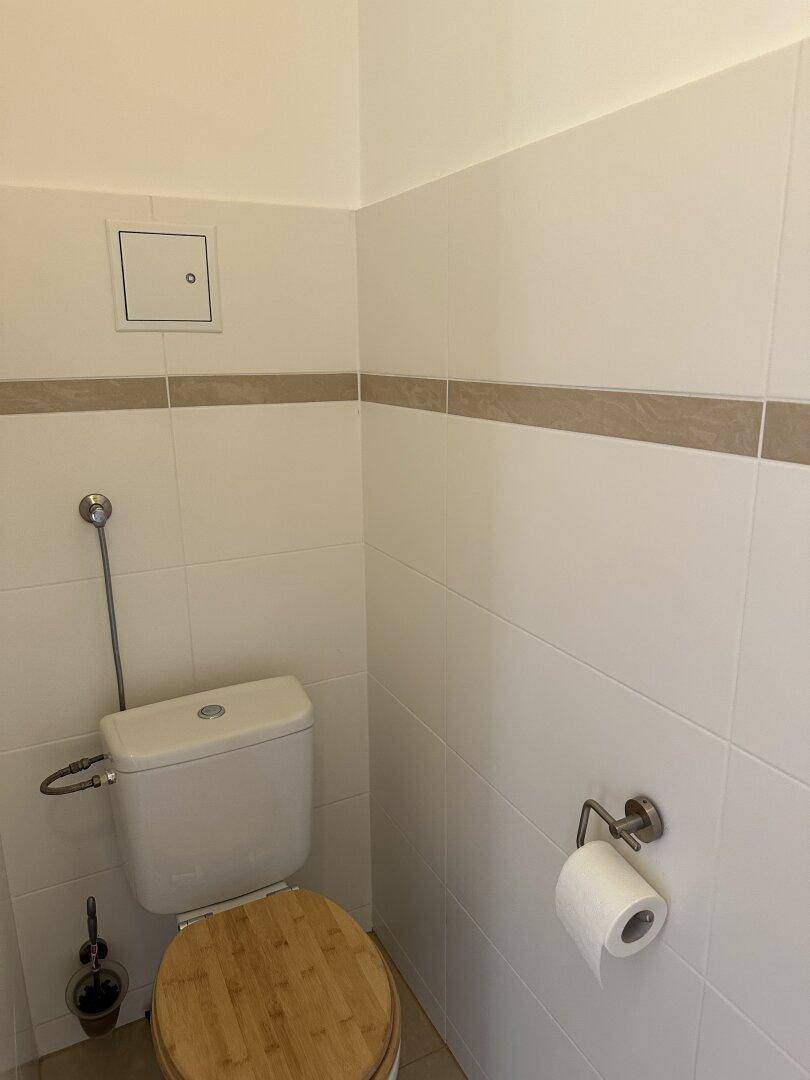 Kleines WC mit weißen Fliesen und einer Toilette mit Holzdeckel.