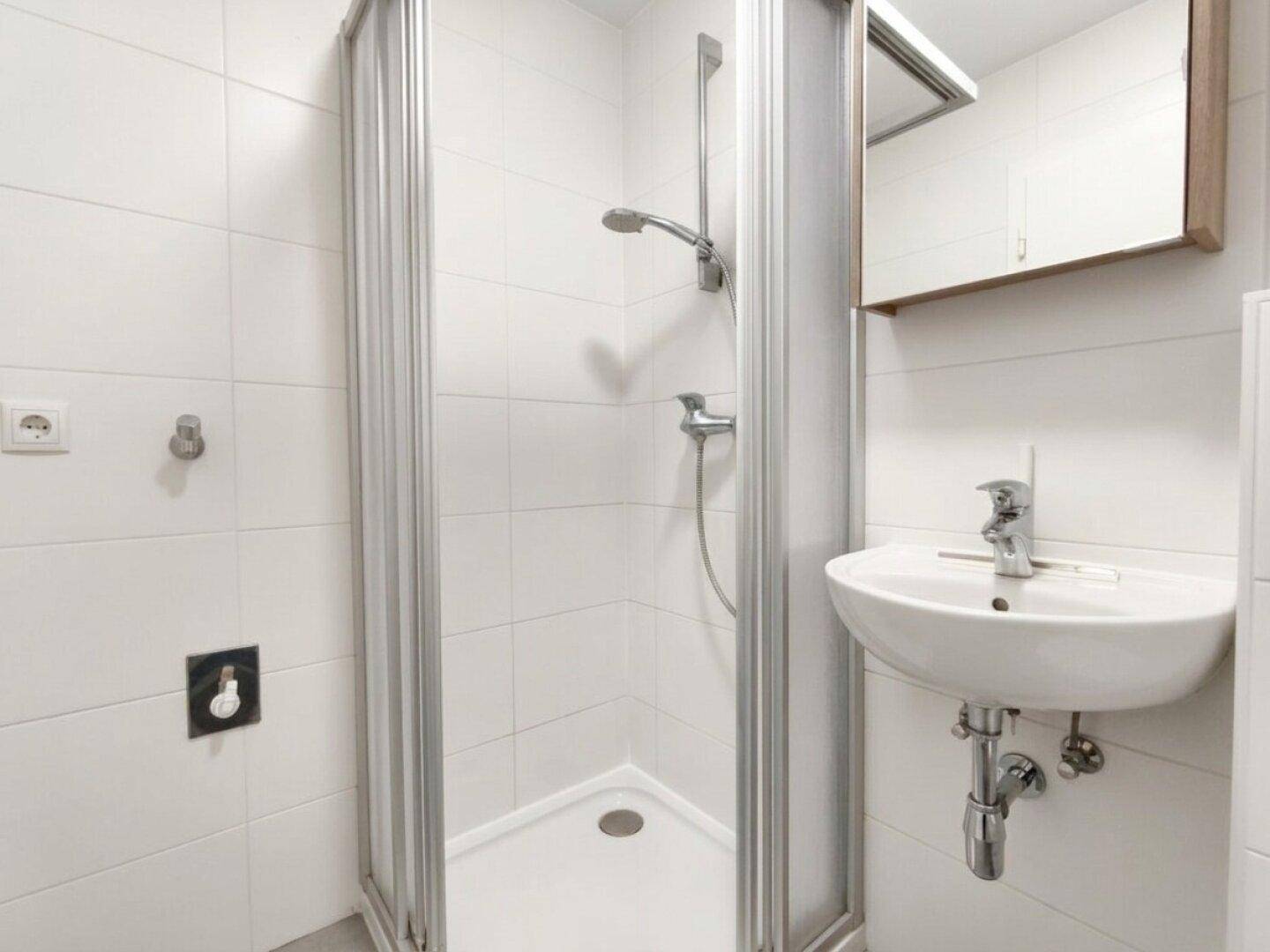 Modernes Badezimmer mit Duschkabine, Waschbecken, Spiegelschrank und weißen Fliesen.