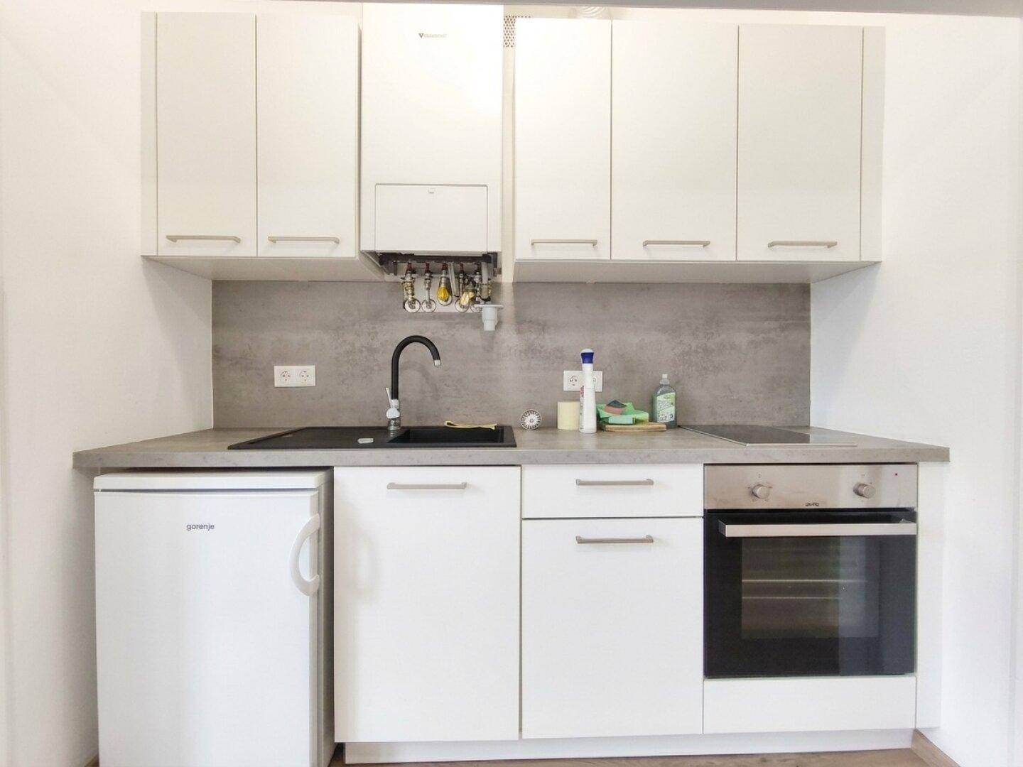 Moderne Küchenzeile mit integriertem Backofen, Kühlschrank, Induktionskochfeld und Hängeschränken.