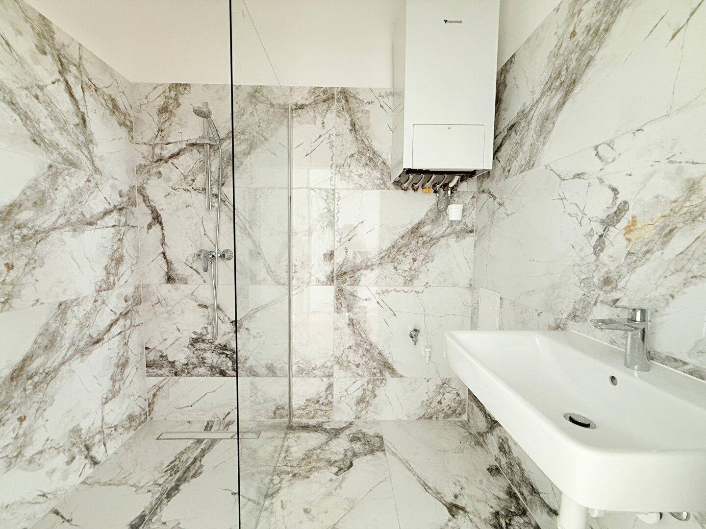 Modernes Badezimmer mit begehbarer Dusche, Waschbecken und stilvollen Marmor-Effekt-Fliesen.