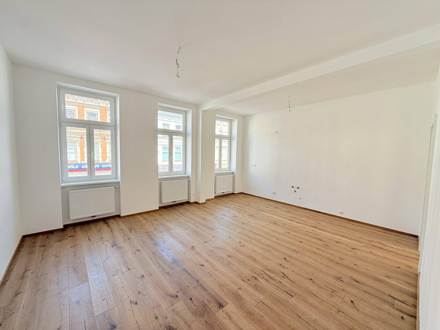 Geräumiger, unmöblierter Raum mit hellem Holzboden und großen Fenstern, ideal für Wohnzwecke.