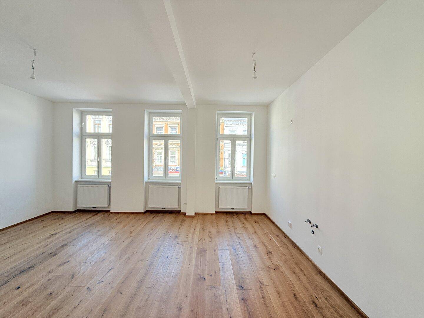Lichtdurchfluteter Raum mit neu verlegtem Holzboden und hohen Fenstern, bietet vielseitige Nutzungsmöglichkeiten.