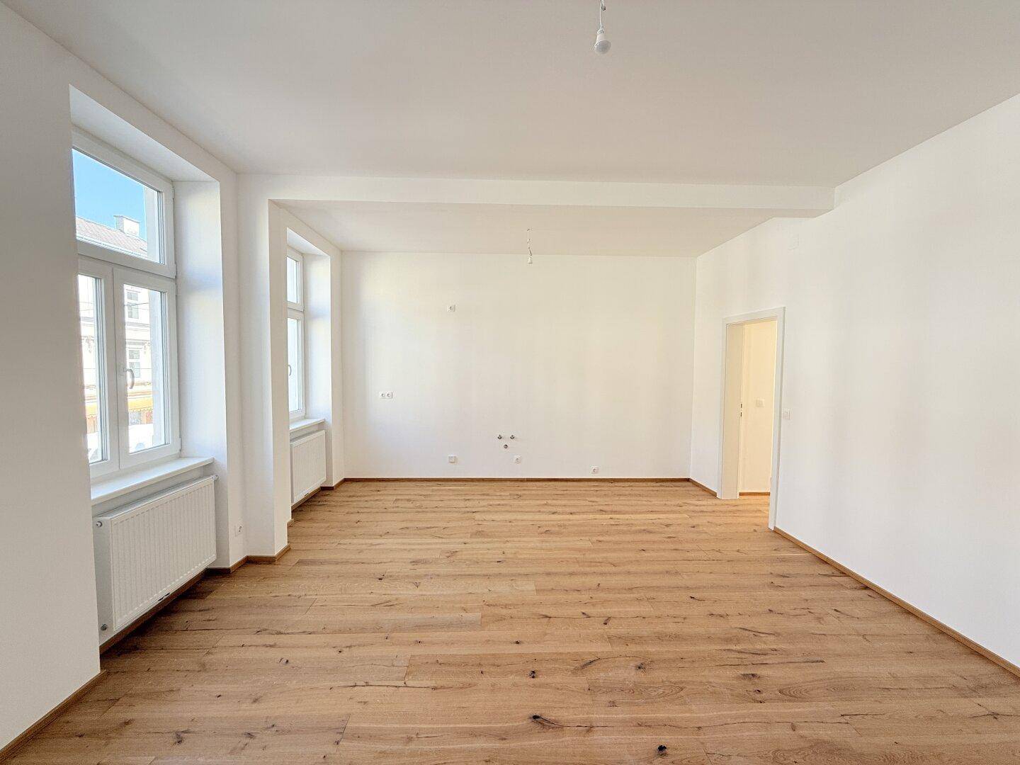Heller, leerer Raum mit neuem Holzboden und weißen Wänden, bereit zur individuellen Gestaltung.
