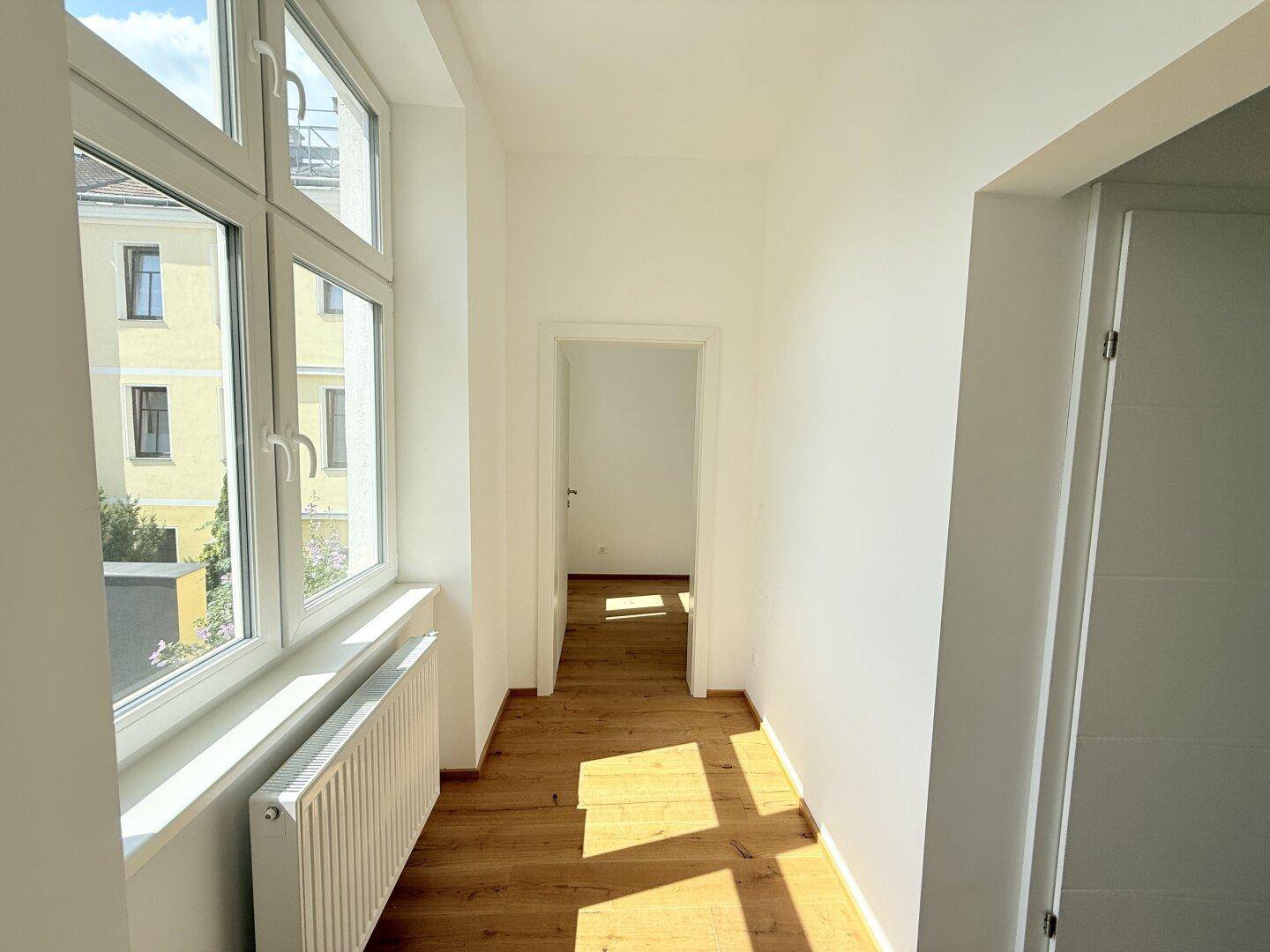 Heller Flur mit Holzboden und großem Fenster, das viel Tageslicht hereinlässt.
